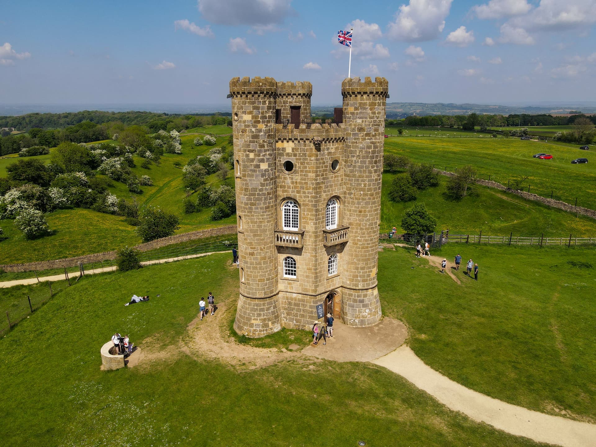 Drone view of Broadway Tower with Union Jack flag flying over green English countryside.