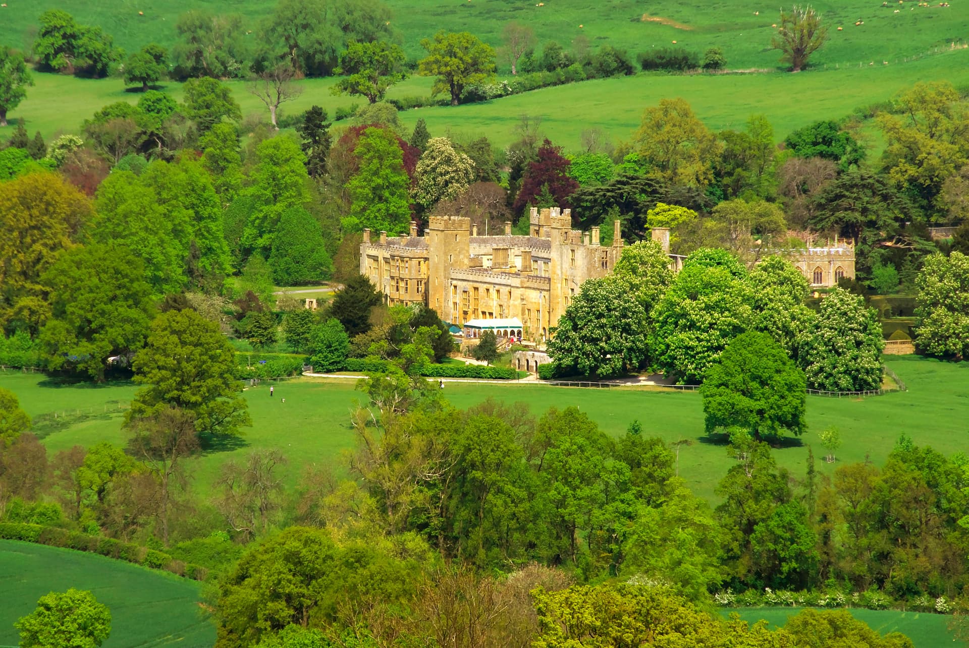 Sudeley Castle surrounded by lush green fields and dense trees in the English countryside.