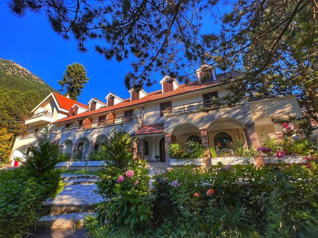Hotel building with red tile roof and garden surrounded by mountains and pine trees