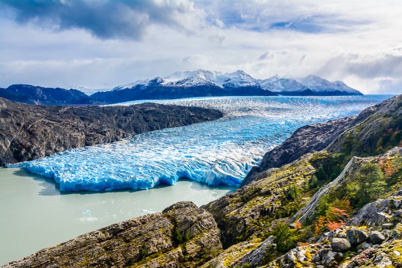 Large blue glacier flowing into a glacial lake surrounded by mountains and rocky terrain