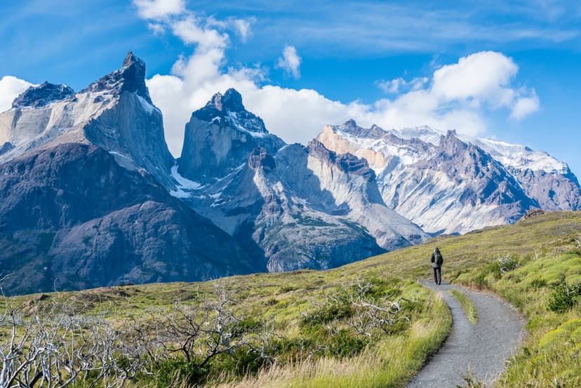 Hiker walking on mountain trail with snow-capped peaks in background