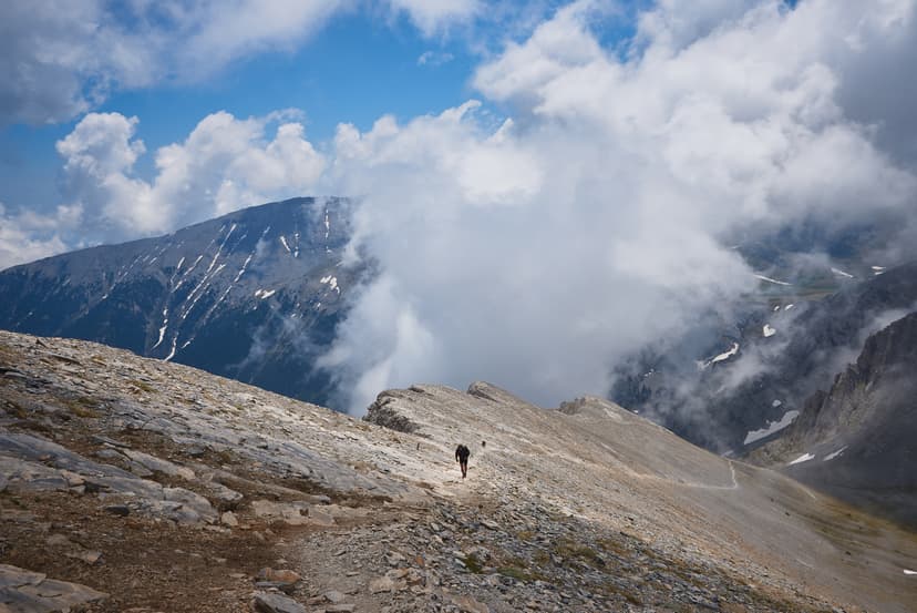 Hiker on rocky mountain trail with clouds and peaks