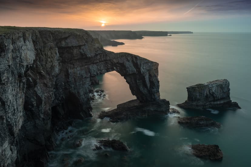 Rock arch formation on coastal cliffs at sunset with ocean water