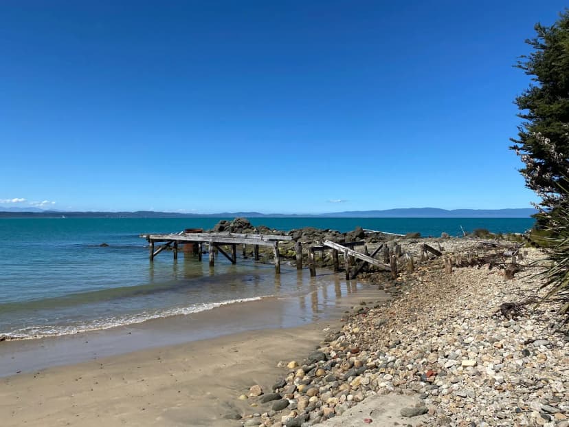 Ruined wooden pier on a stony beach at Port Craig with turquoise water and blue sky