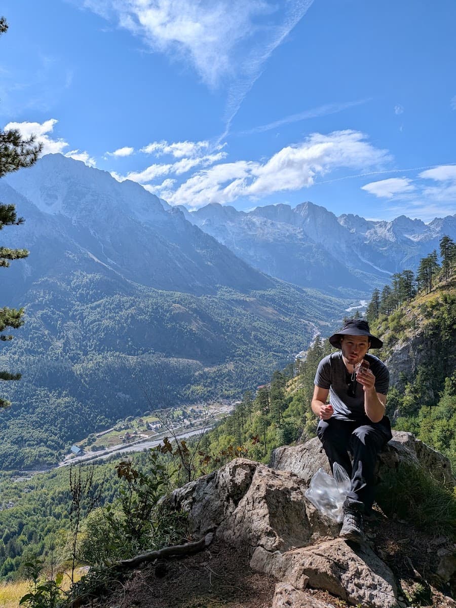 Hiker sitting on a rock eating snack with mountain valley landscape background