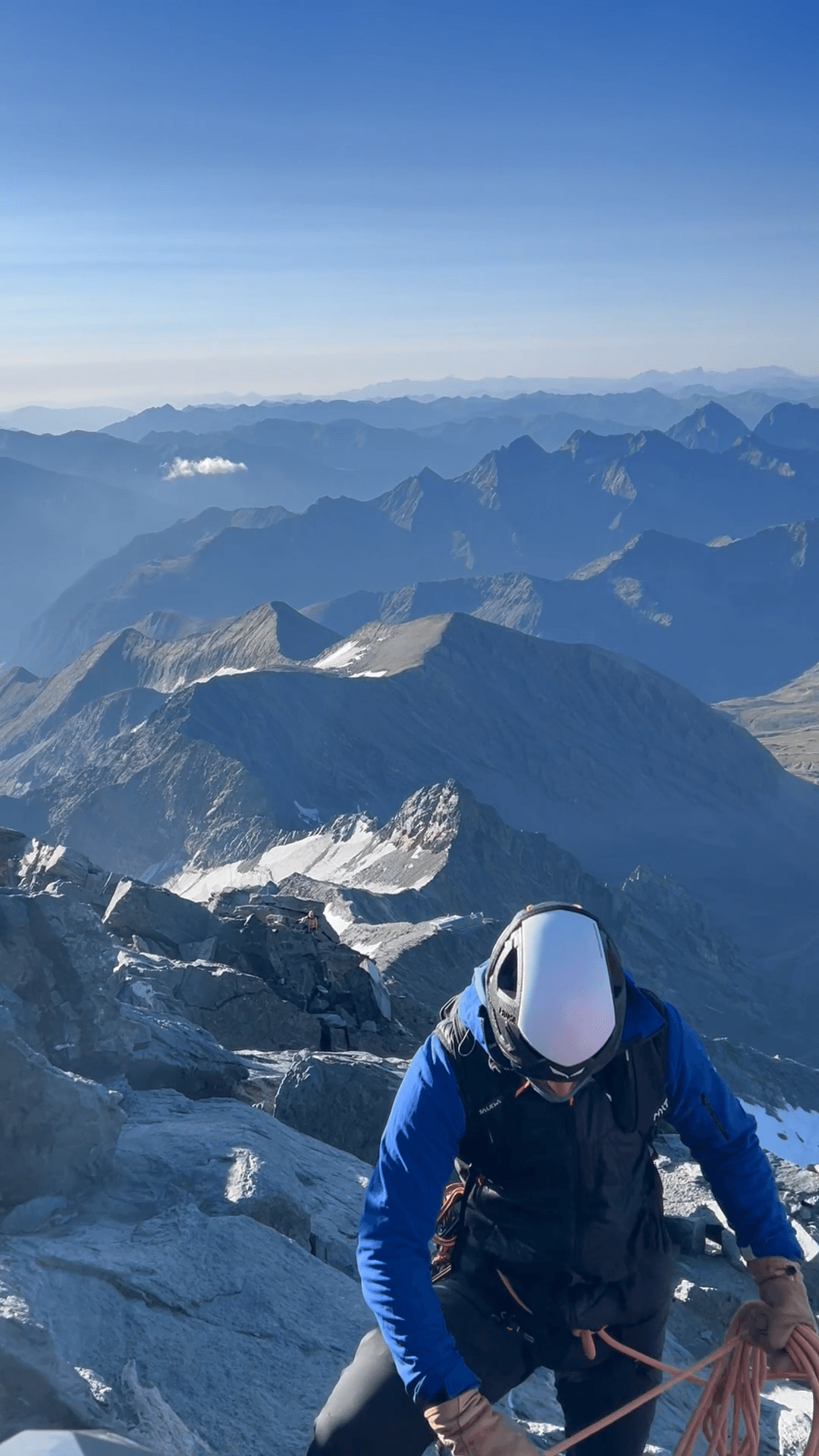 Mountaineer climbing rocky alpine ridge with mountain range in background