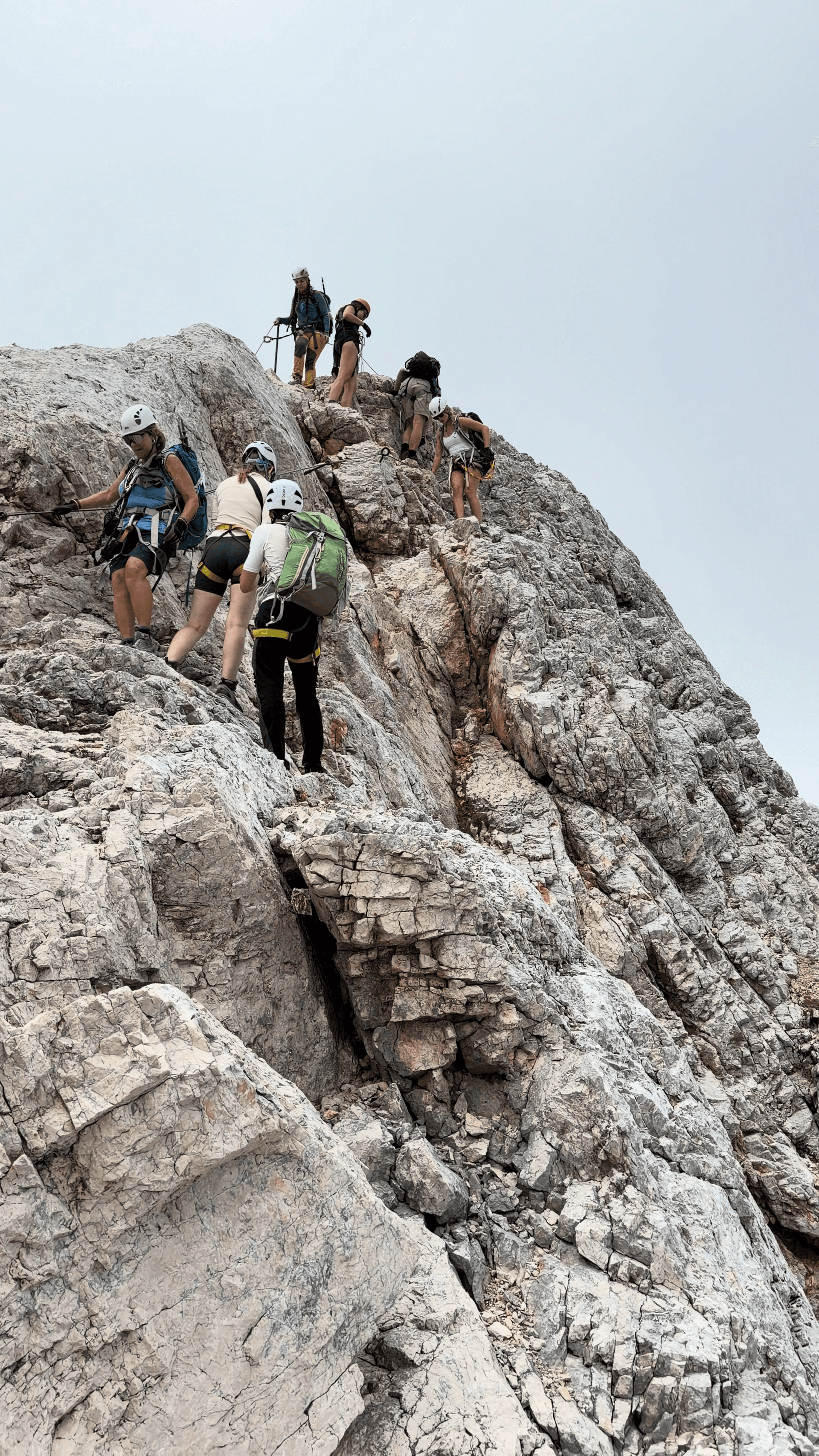 Hikers ascending a steep rocky mountain ridge wearing helmets and safety harnesses