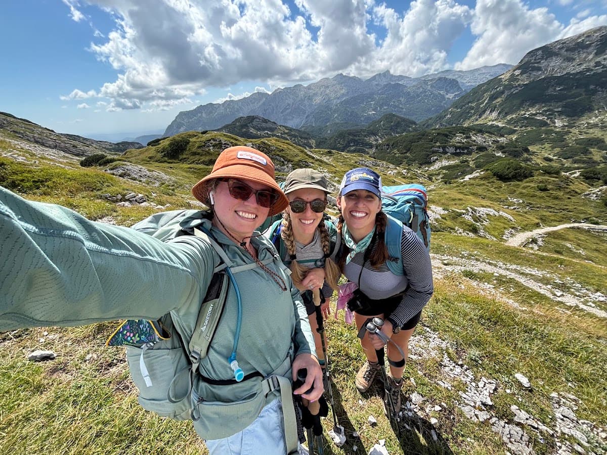 Three hikers taking a selfie on a mountain trail with alpine peaks