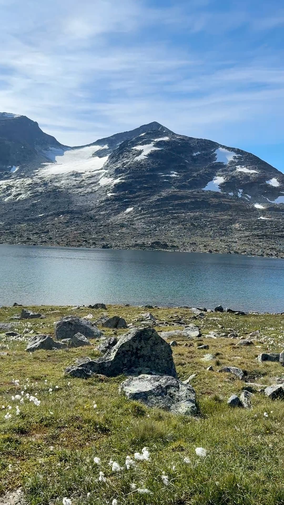 Alpine lake with rocky shore and snow-dusted mountain peaks under blue sky