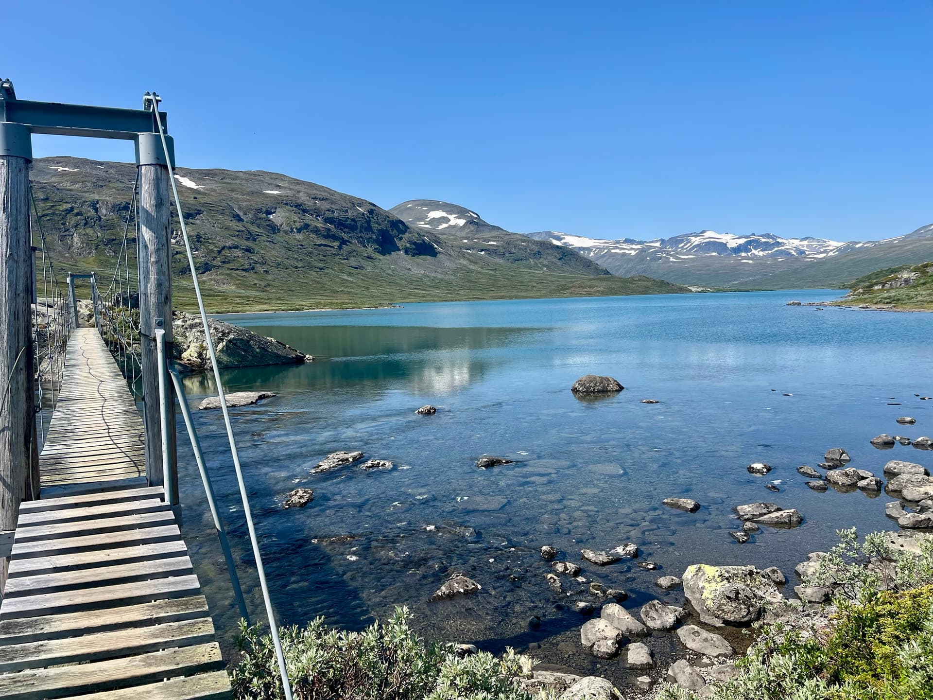 Suspension bridge over a clear lake with mountains in the background