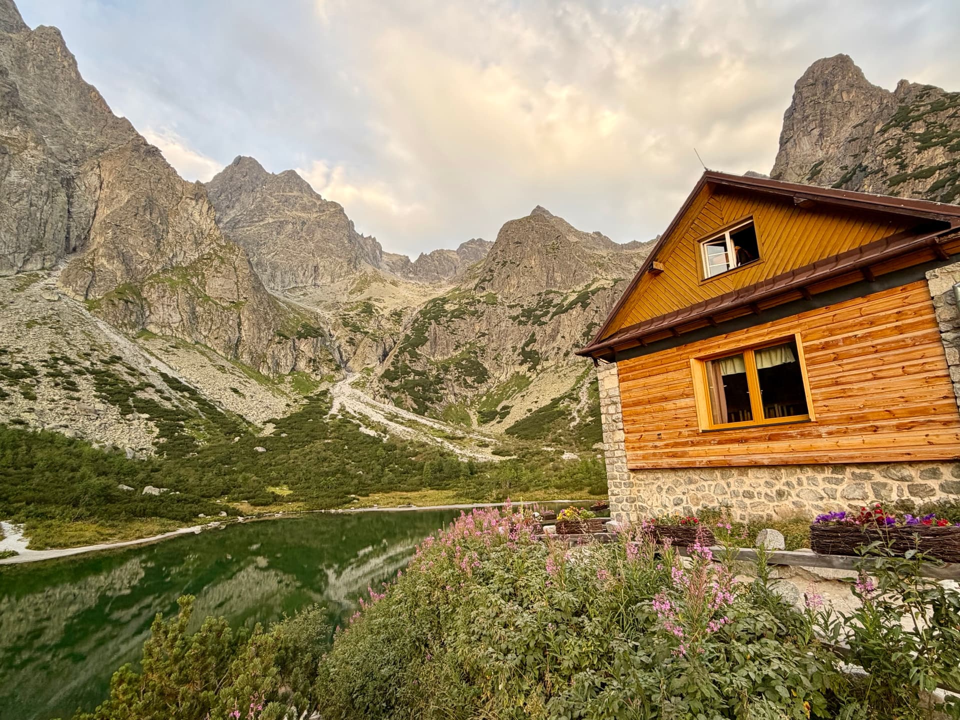 Wooden hut beside a mountain lake with rocky peaks in the background