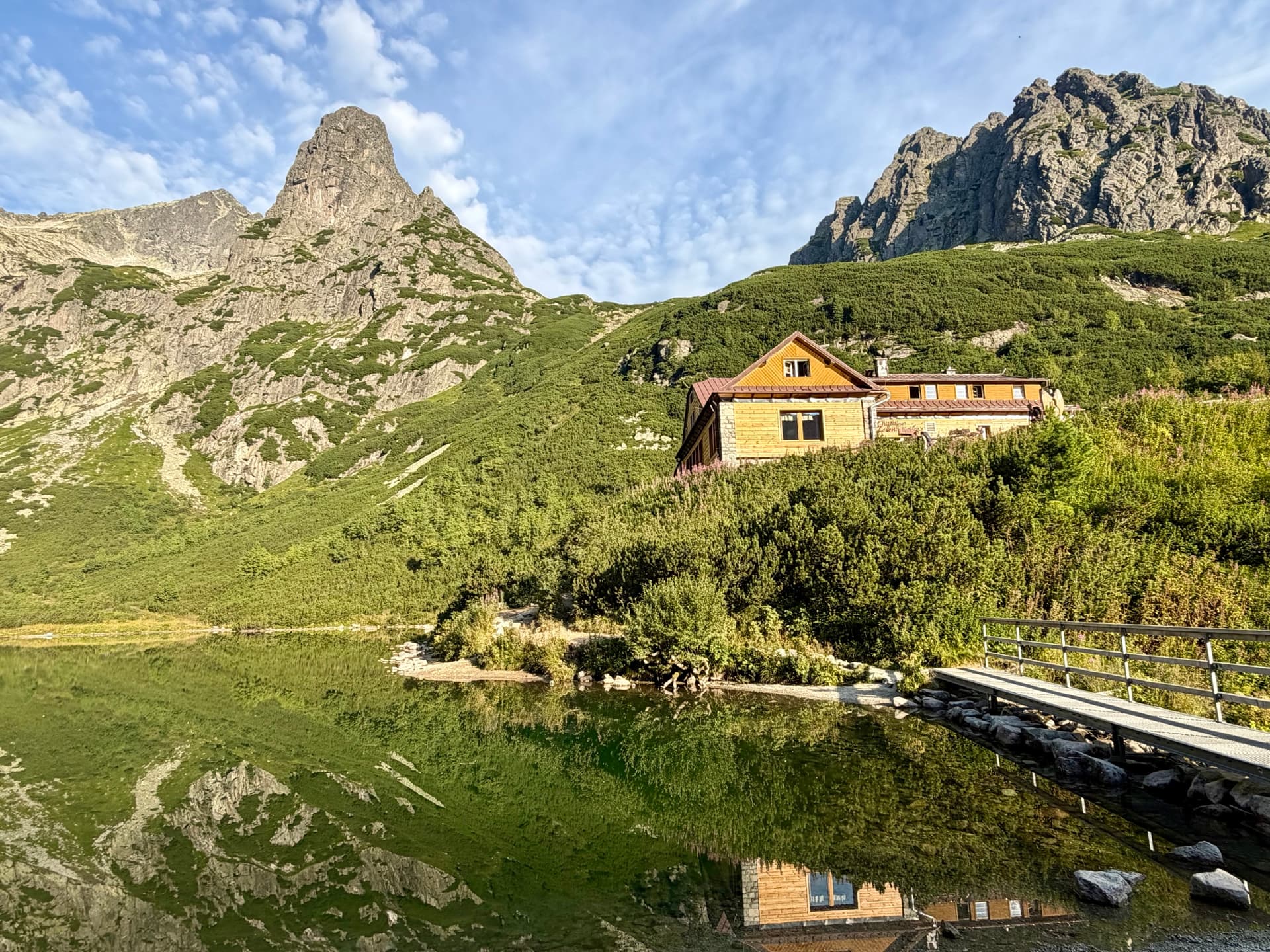 Wooden alpine hut reflected in still mountain lake with rocky peaks