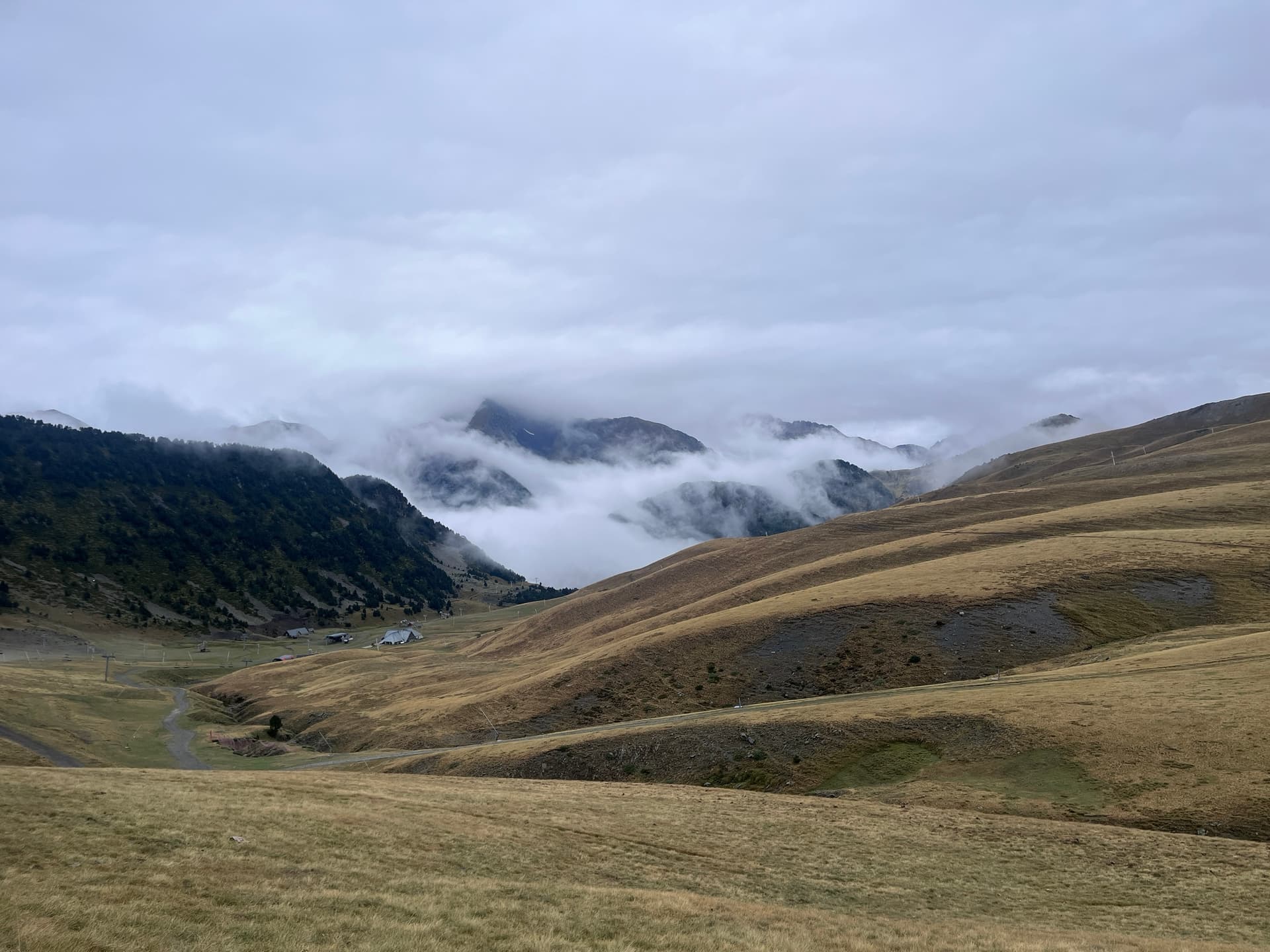 Low clouds over a grassy alpine valley with distant mountains