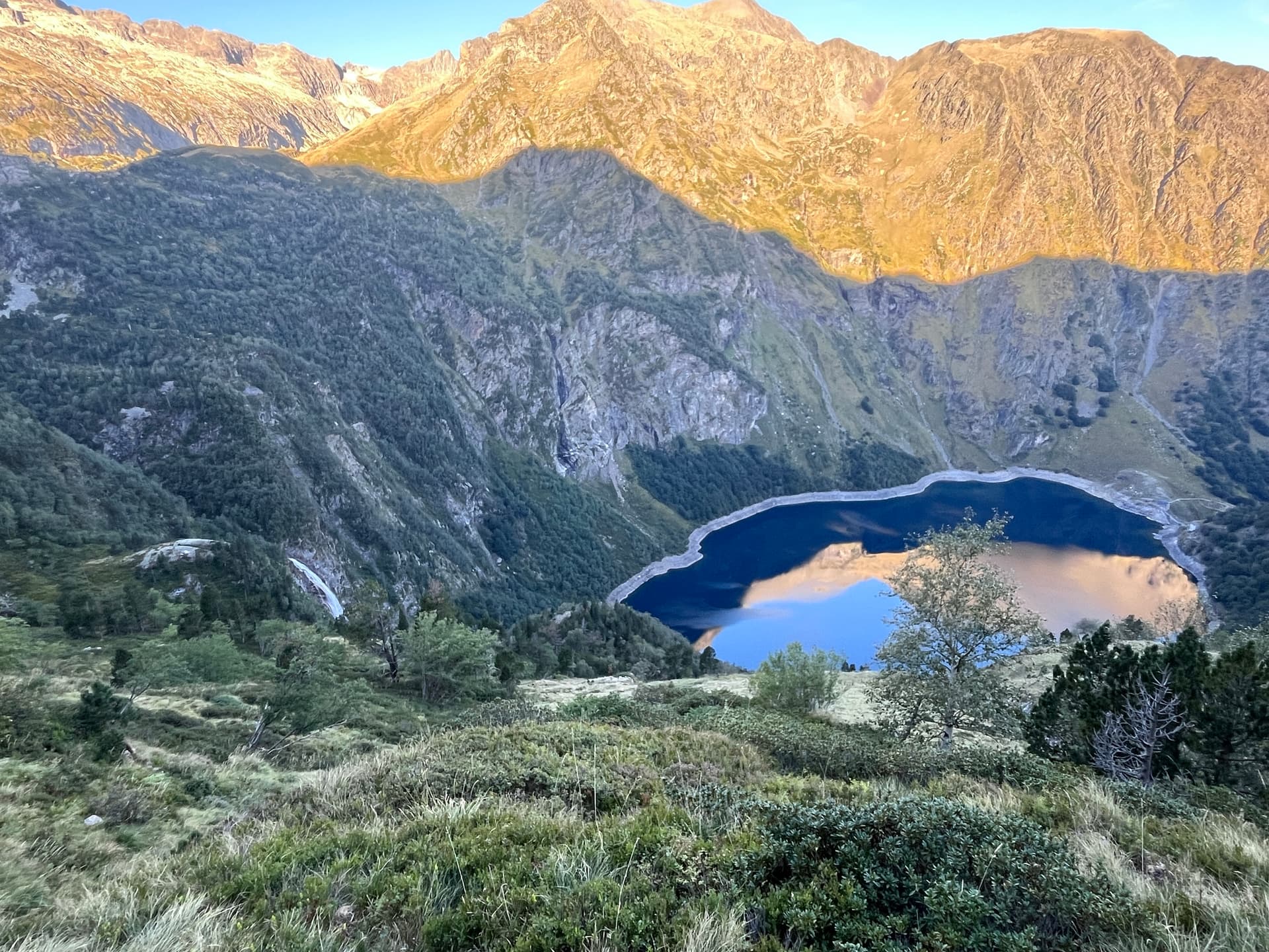 Alpine lake below rugged mountain peaks illuminated by morning sun