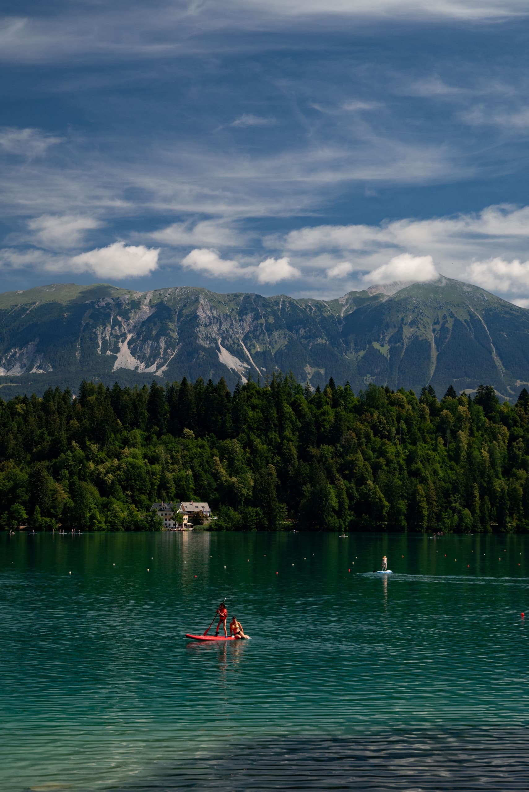 Paddleboarders on a turquoise alpine lake with forested shoreline and mountains