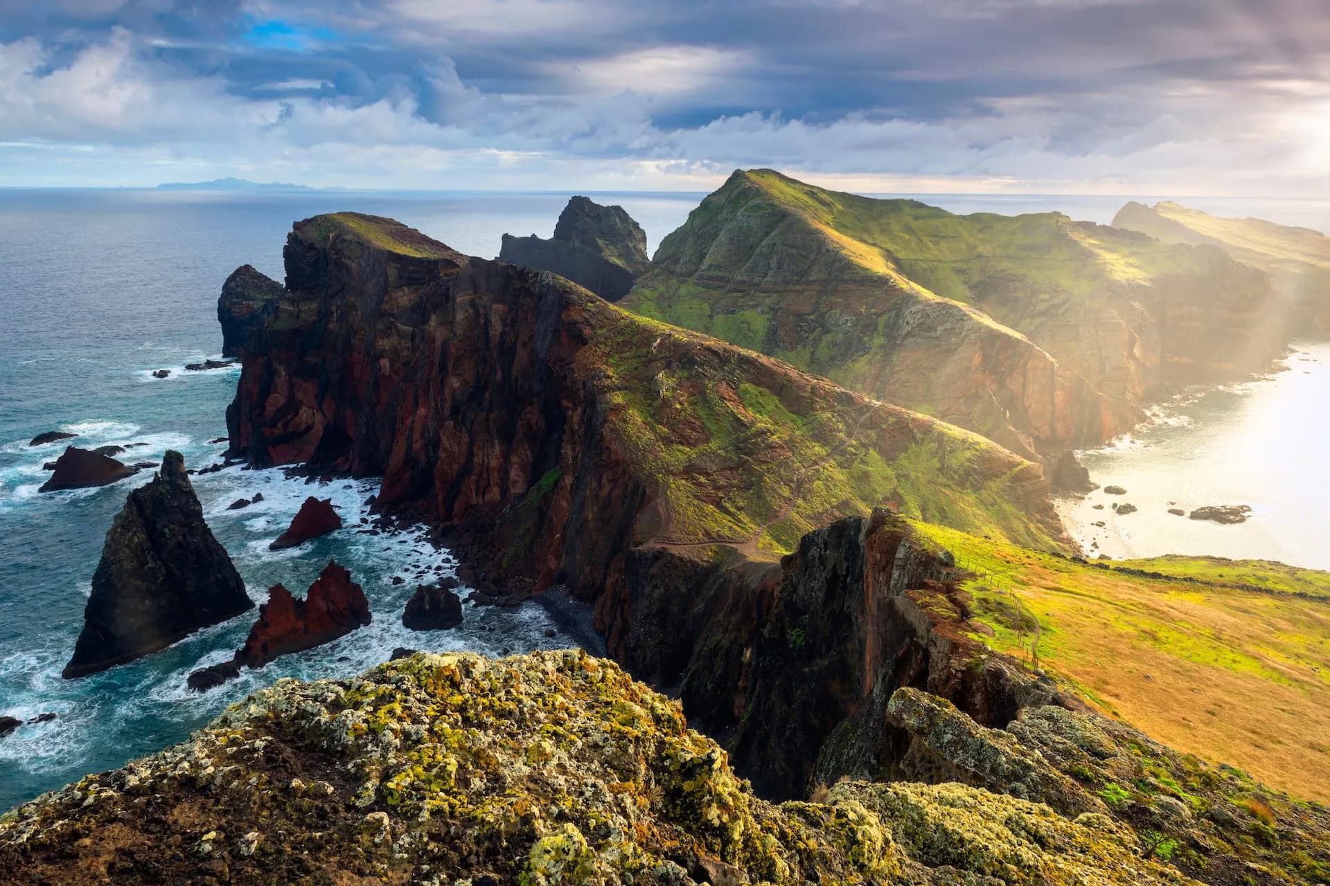 Rugged green and brown cliffs meeting the ocean at Ponta de São Lourenço on Madeira under dramatic sky.