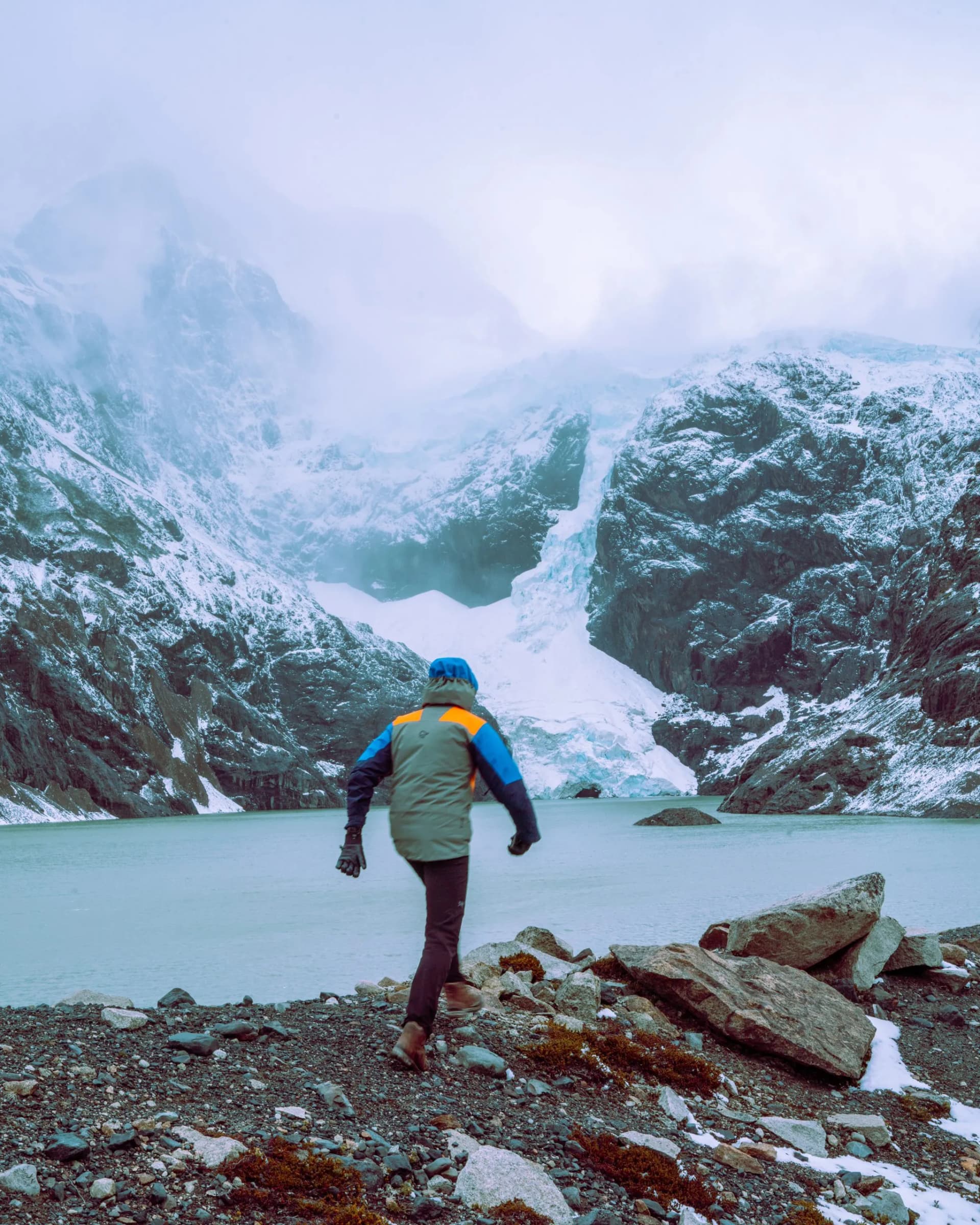Hiker approaches Glaciar Los Perros with glacial lake and snow-covered mountains.