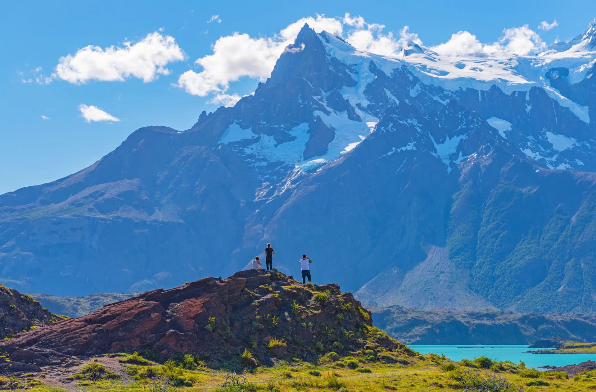 Hikers viewing snow-capped mountains above turquoise water at Lake Nordenskjöld.