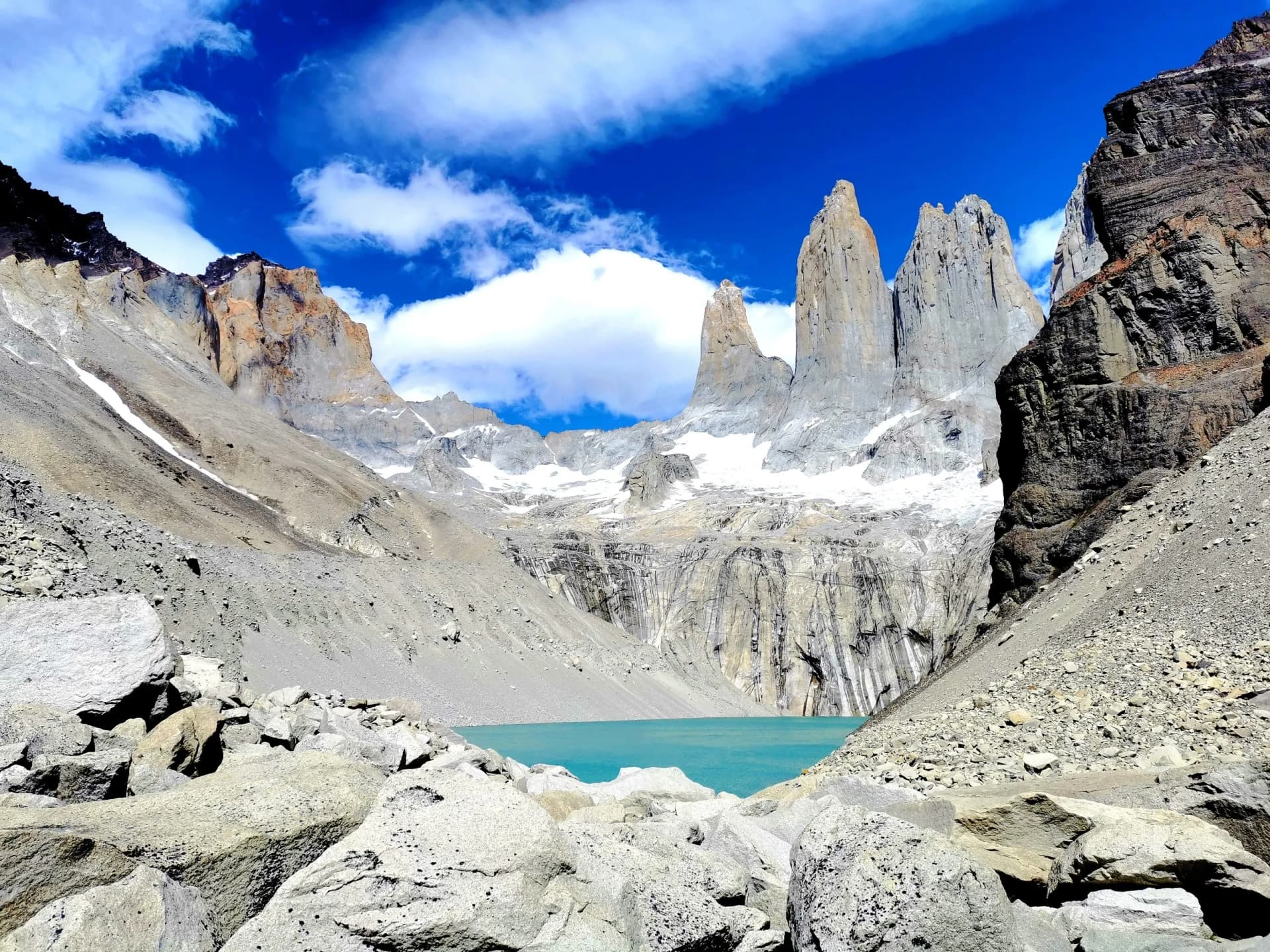 Jagged granite peaks above turquoise glacial lake surrounded by scree and boulders under blue sky.