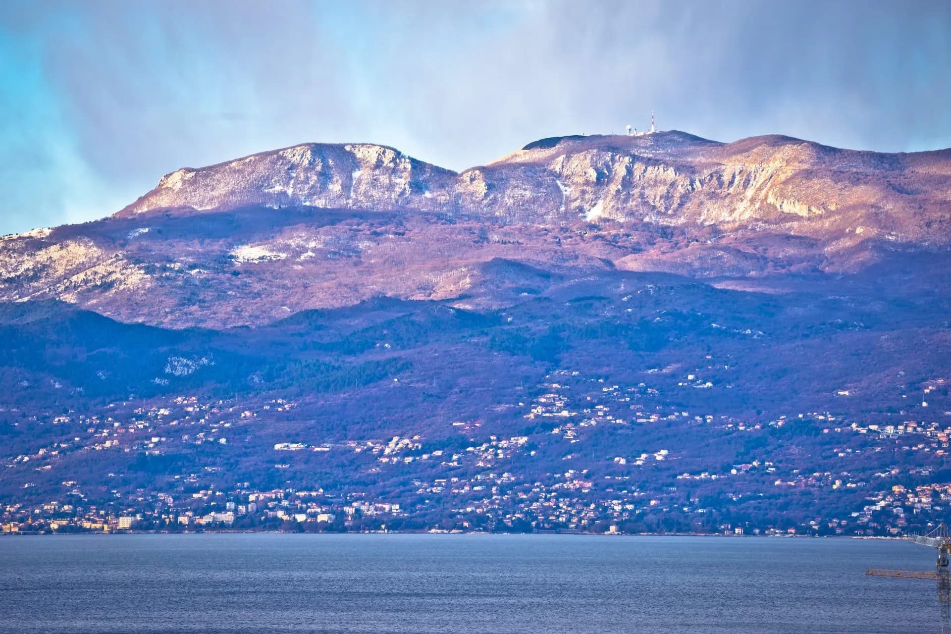 Coastal town nestled below snow-dusted mountains above the sea in Kvarner-Istria region.
