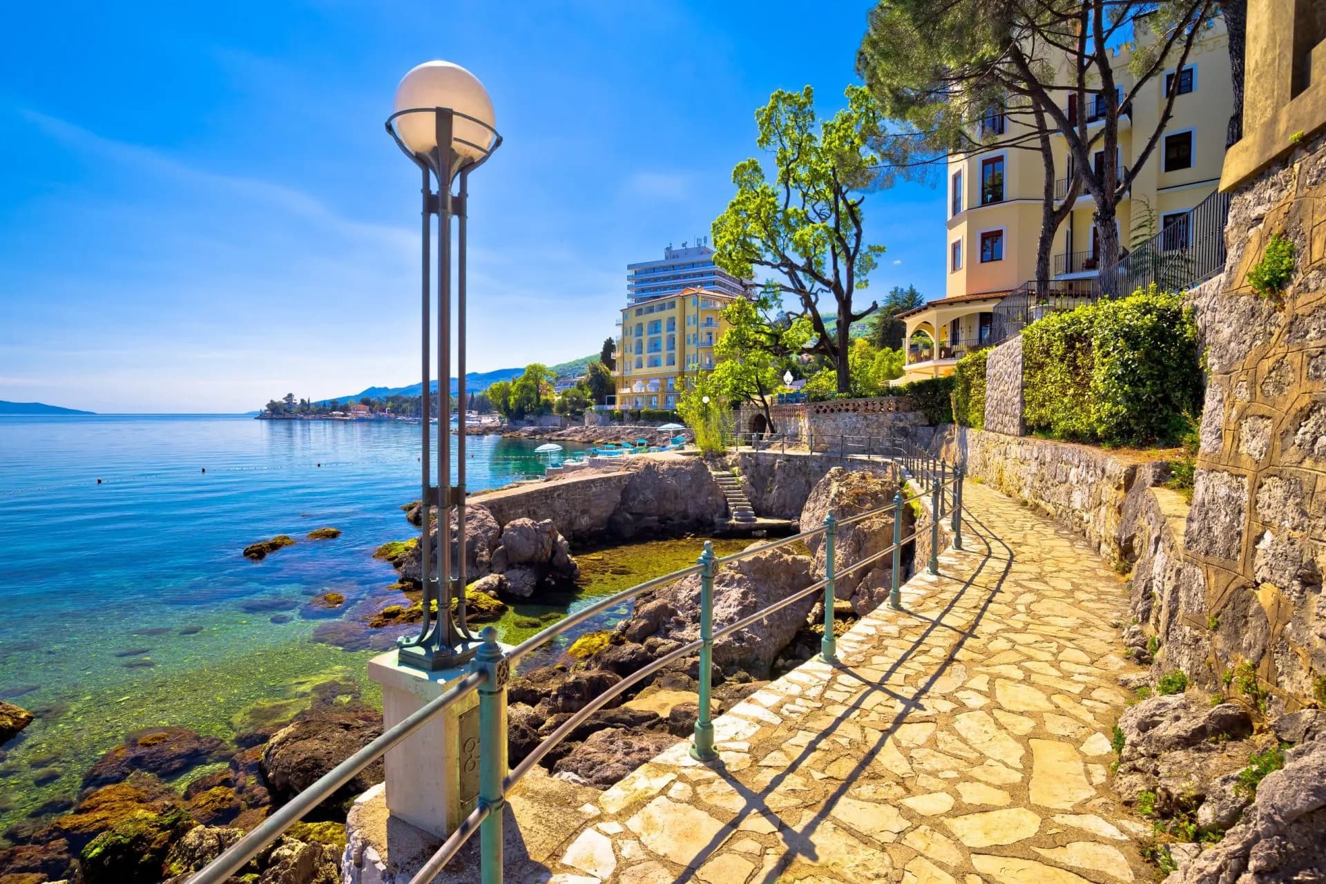 Lungomare walkway in Opatija along the rocky Adriatic coastline with clear blue water.