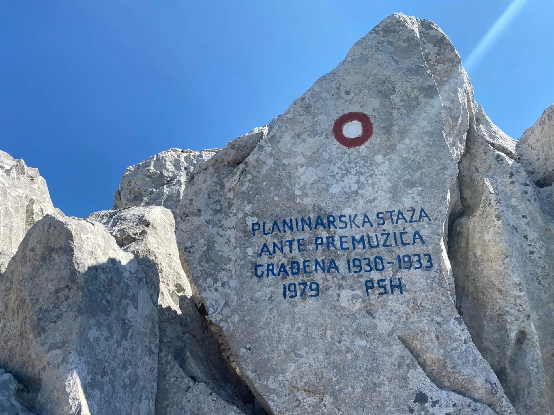 Hiking trail marker painted on large limestone rock under clear blue sky on Premužić Trail