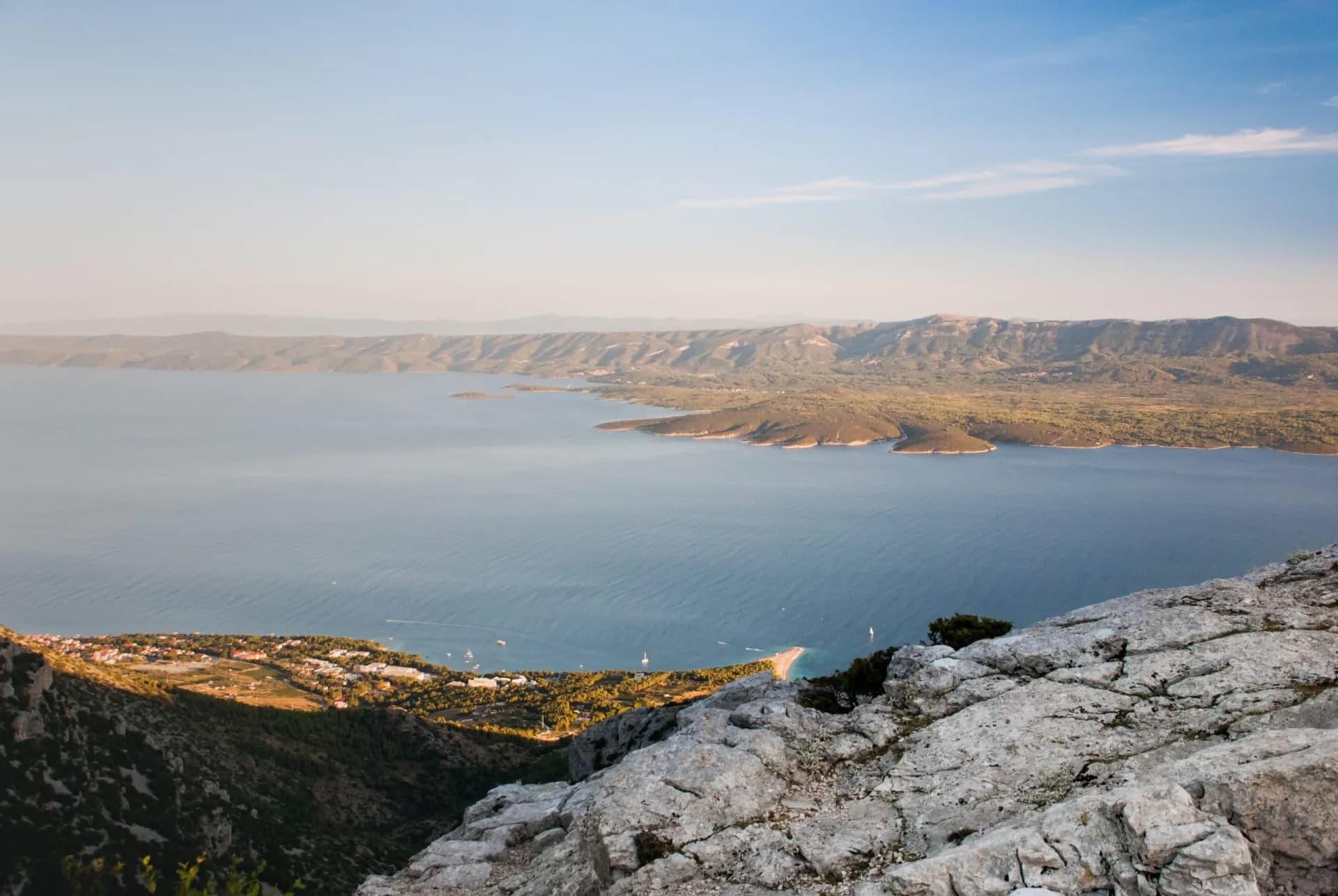 Hiking view from rocky peak over coastal town, blue sea, and distant mountains in Croatia.