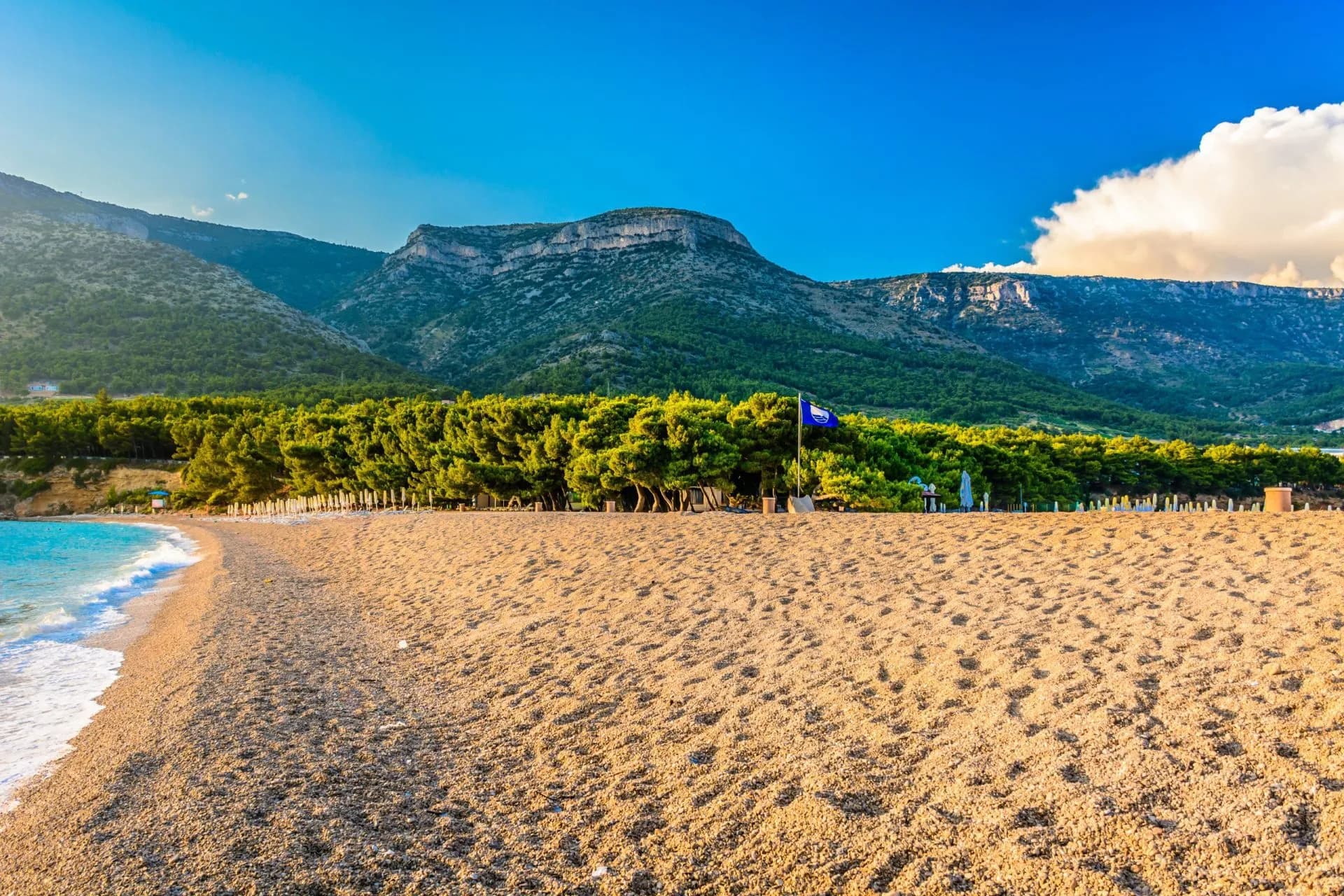 Pebble beach meeting turquoise water below green, scrub-covered mountains on the Adriatic coast.
