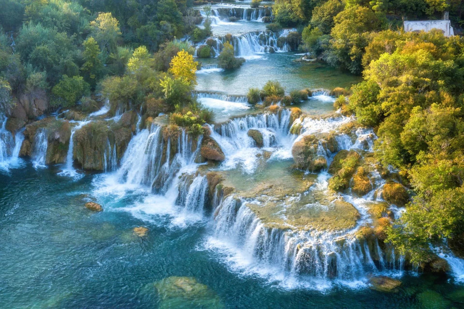 Aerial view of Krka National Park waterfalls cascading over travertine barriers surrounded by lush green forest.