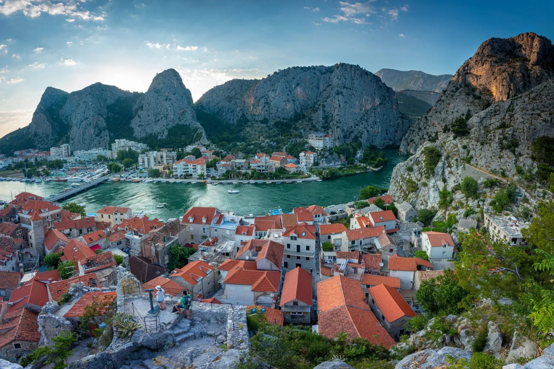 Coastal town with red roofs nestled between steep mountains and a green river, likely Omiš.