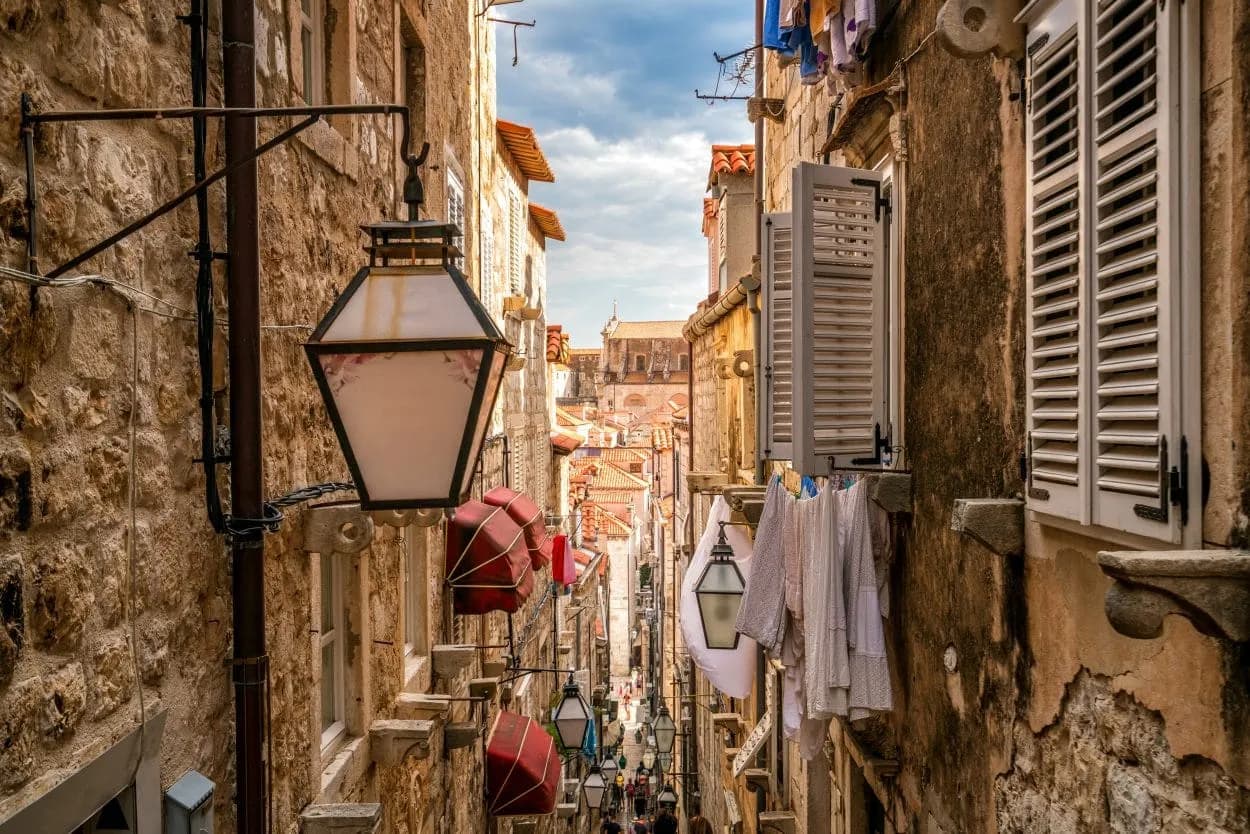 Narrow Dubrovnik street with stone buildings, hanging lanterns, and laundry drying outdoors.