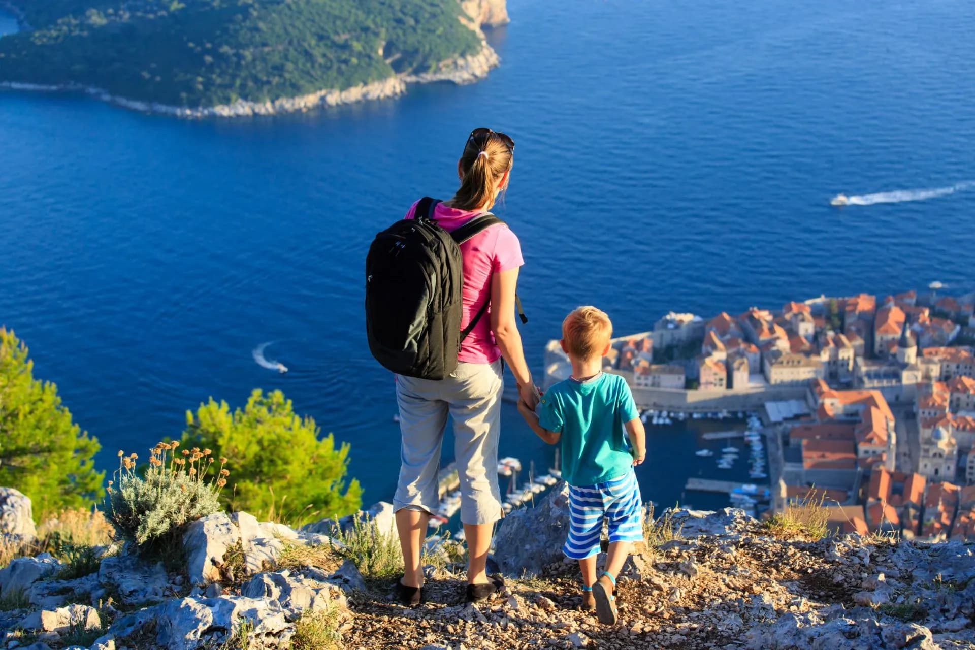 Hikers overlook Dubrovnik's terracotta roofs and blue Adriatic Sea from a rocky viewpoint.