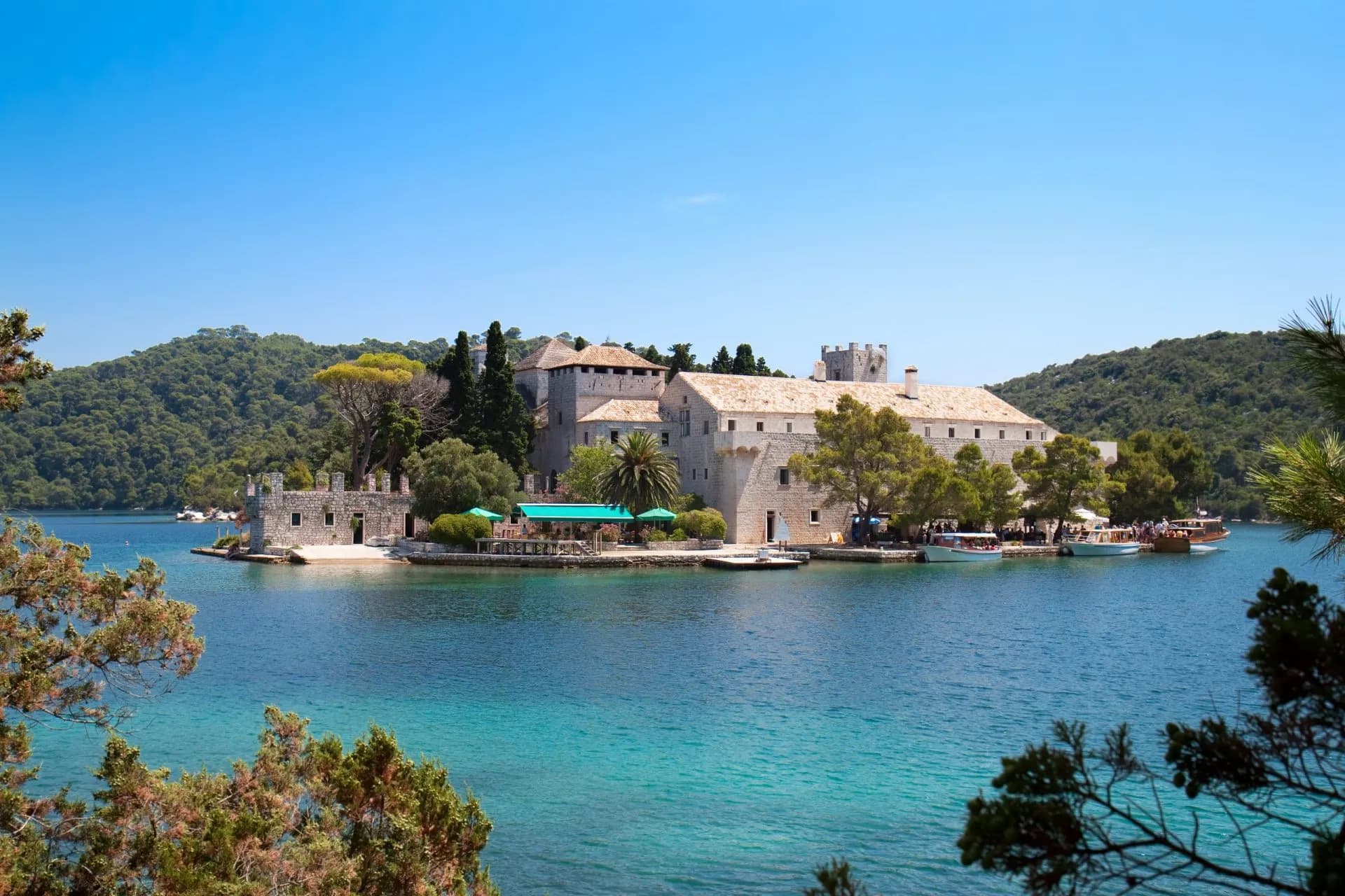 Historic monastery complex on island with boats docked on turquoise water near Mljet Island.