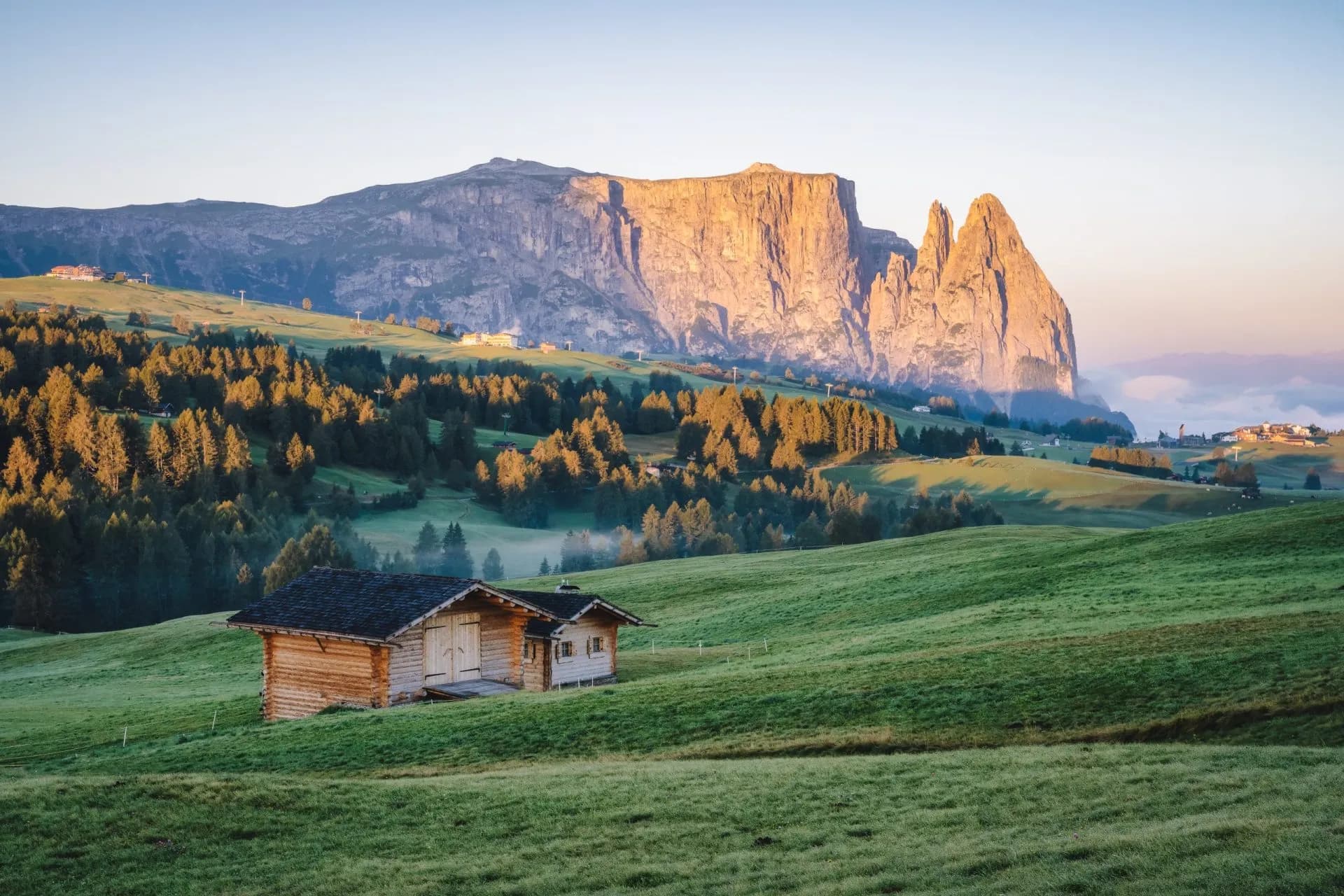 Wooden hut on green Seiser Alm meadow with the Schlern mountain massif in the background.