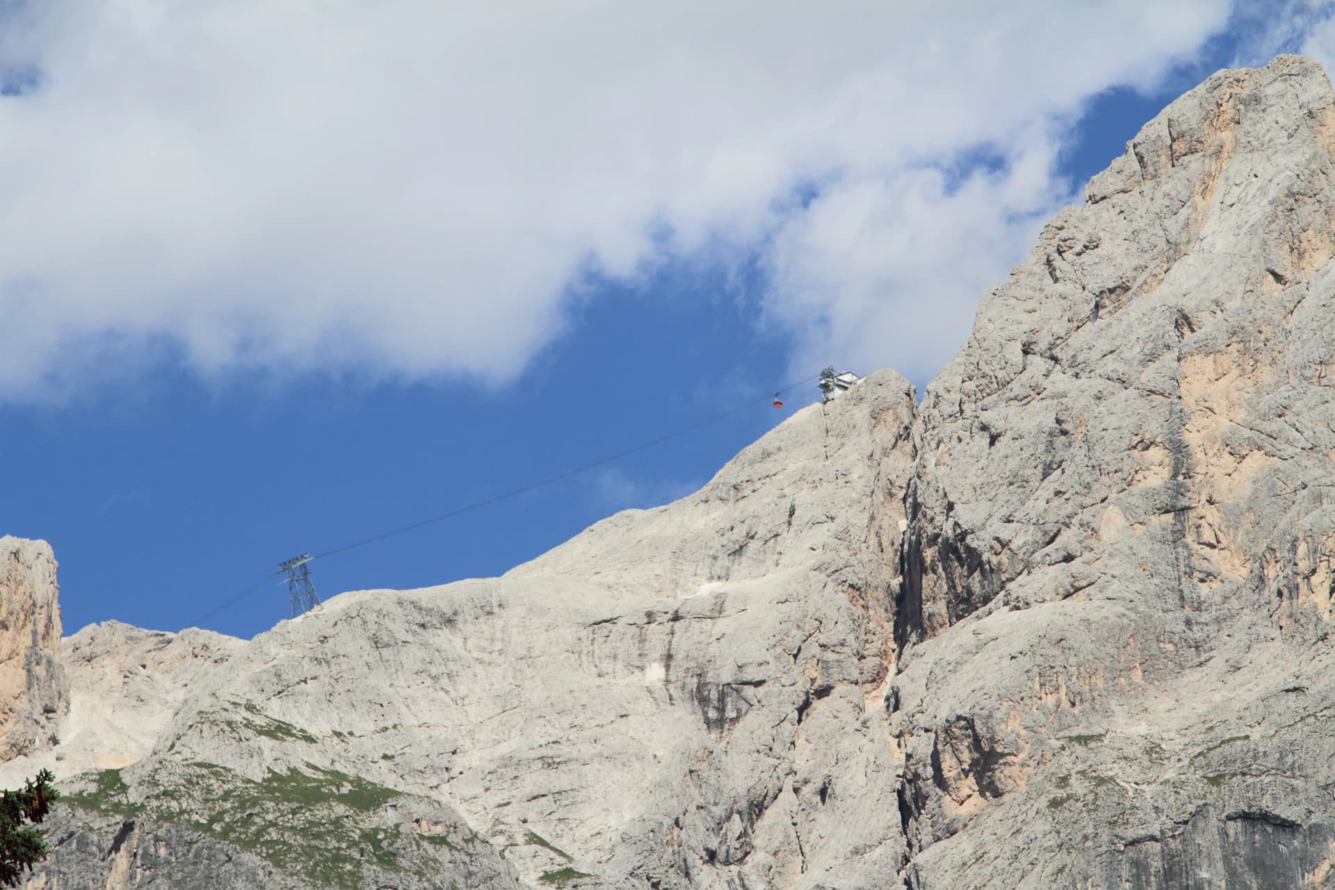 Cable car ascending steep rocky mountain face under blue sky with clouds, Funivia della Rosetta.
