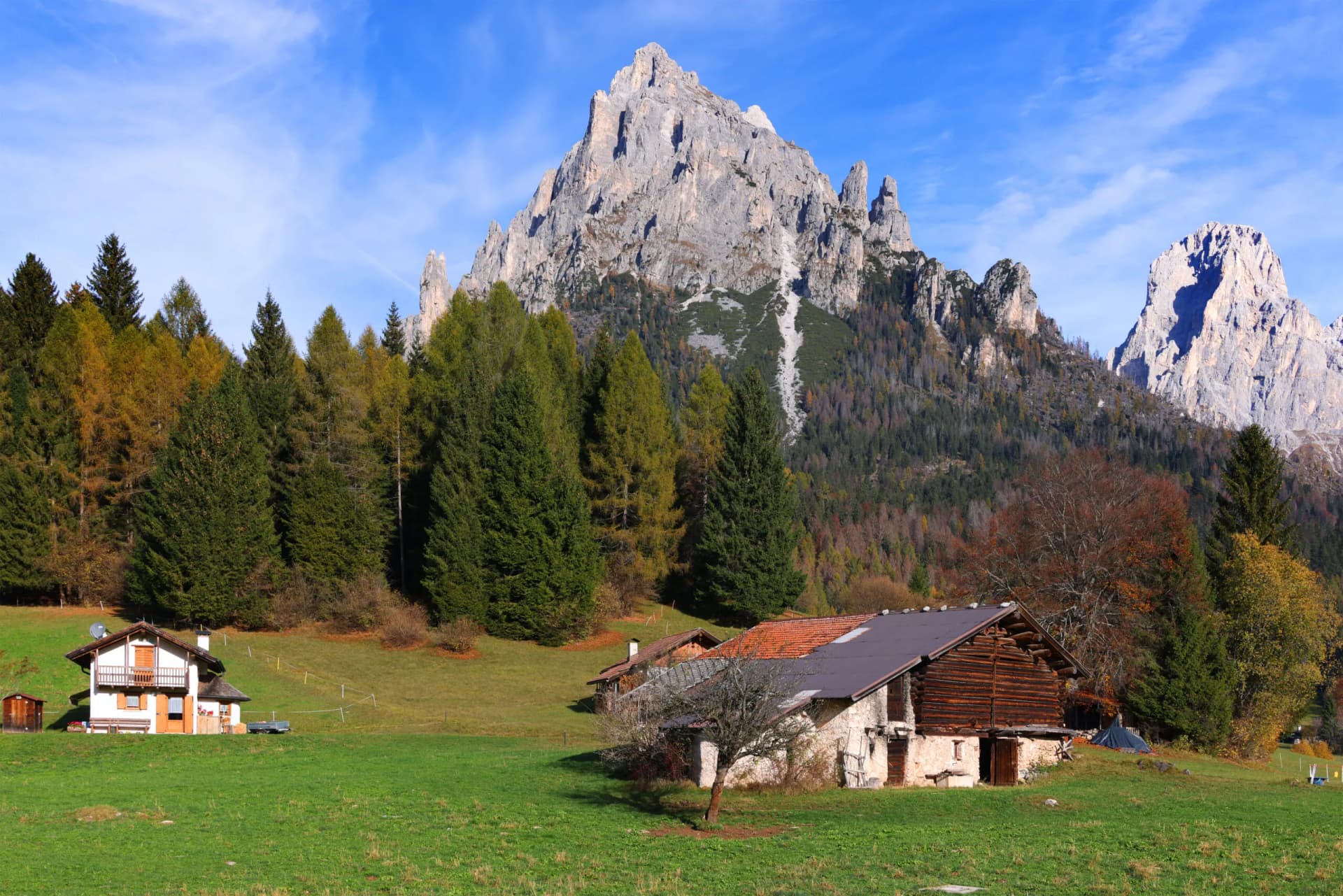 Alpine meadow with rustic farm buildings below jagged peaks near Rifugio Pradidali.