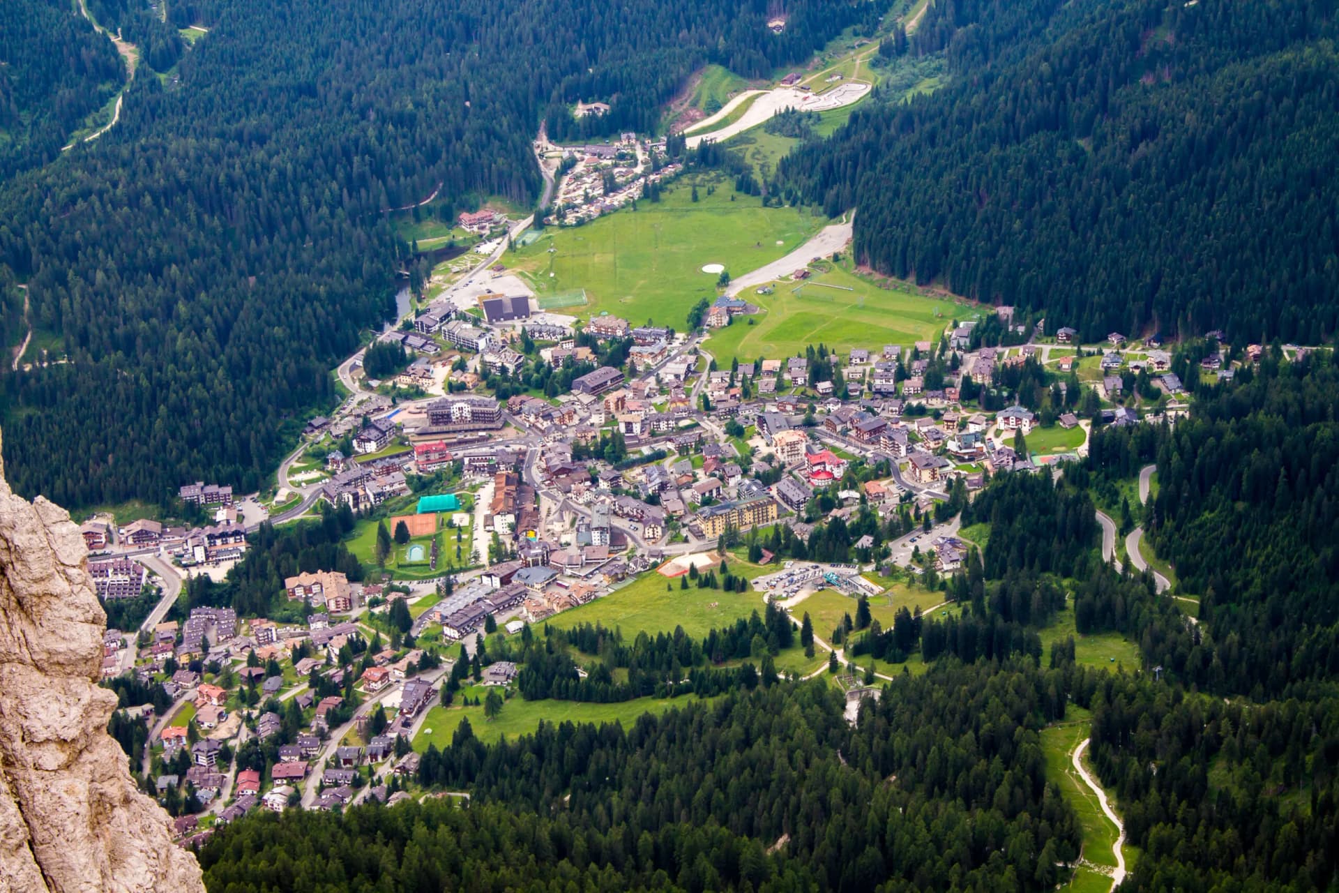 Aerial view of San Martino di Castrozza village nestled in green valley surrounded by dense pine forests.