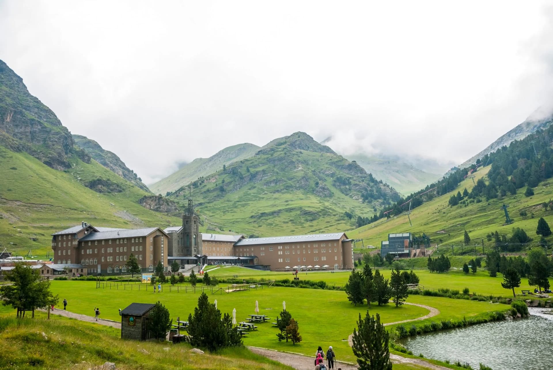 Large building complex in a valley with green mountains and low clouds in summer