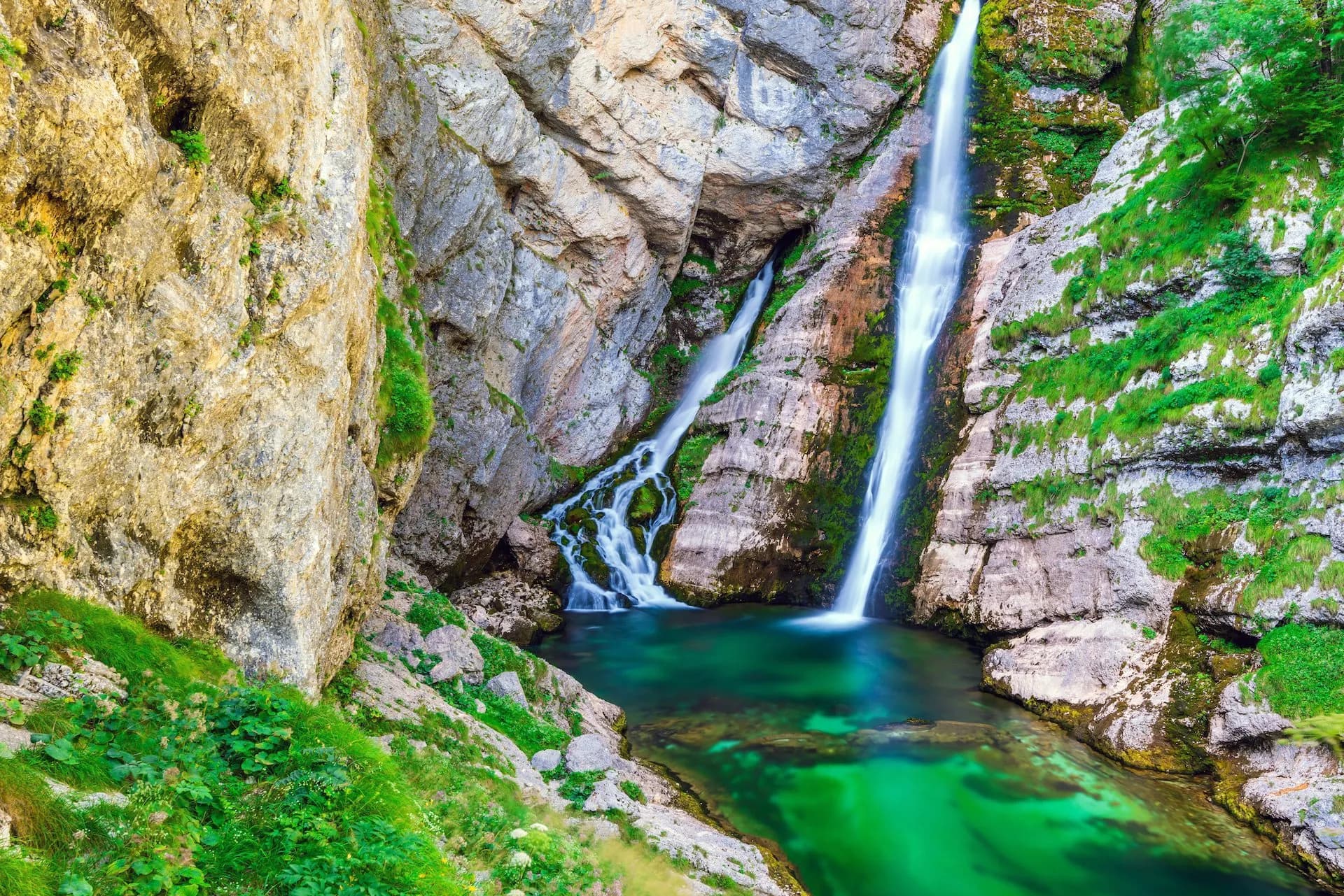 Savica Waterfall cascading down rocky cliffs into a vibrant green pool in the Julian Alps.