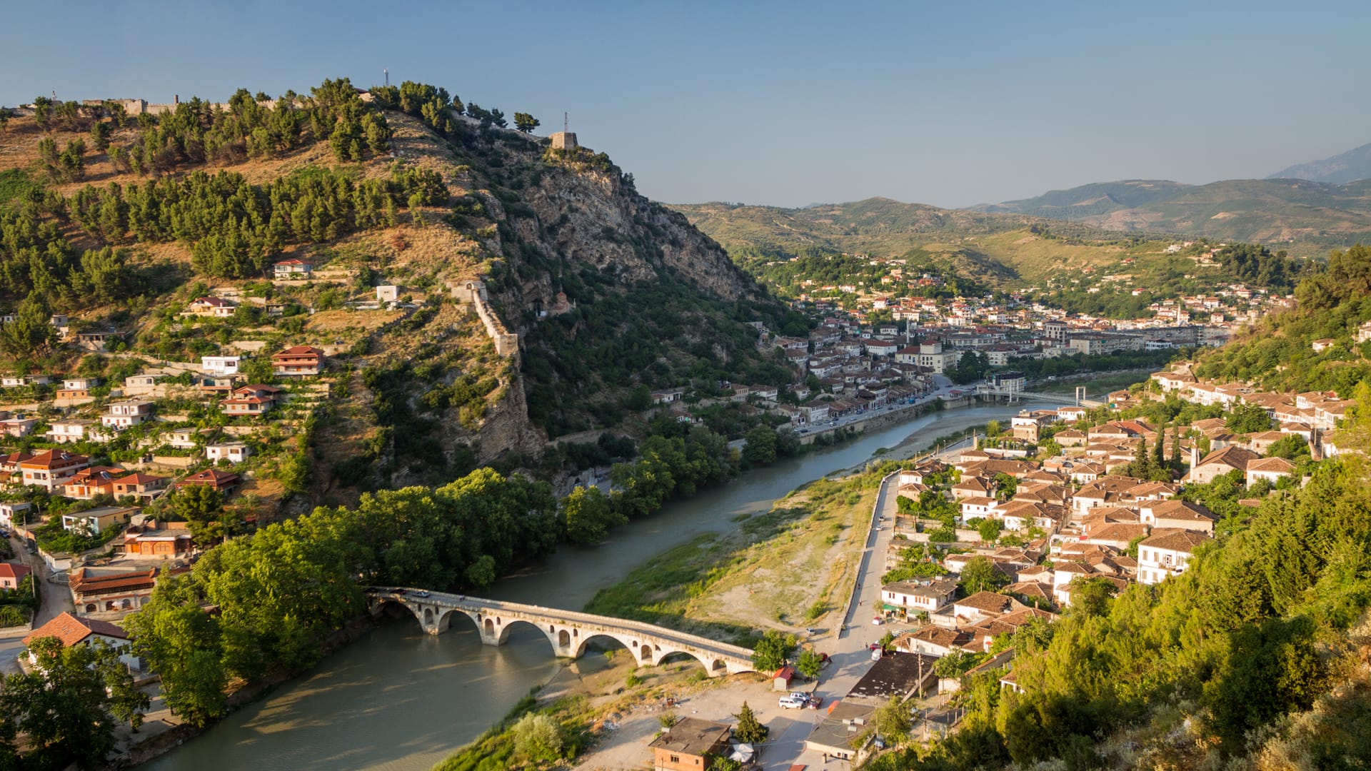 Historic town with stone bridge over river nestled in green hills, Albania.