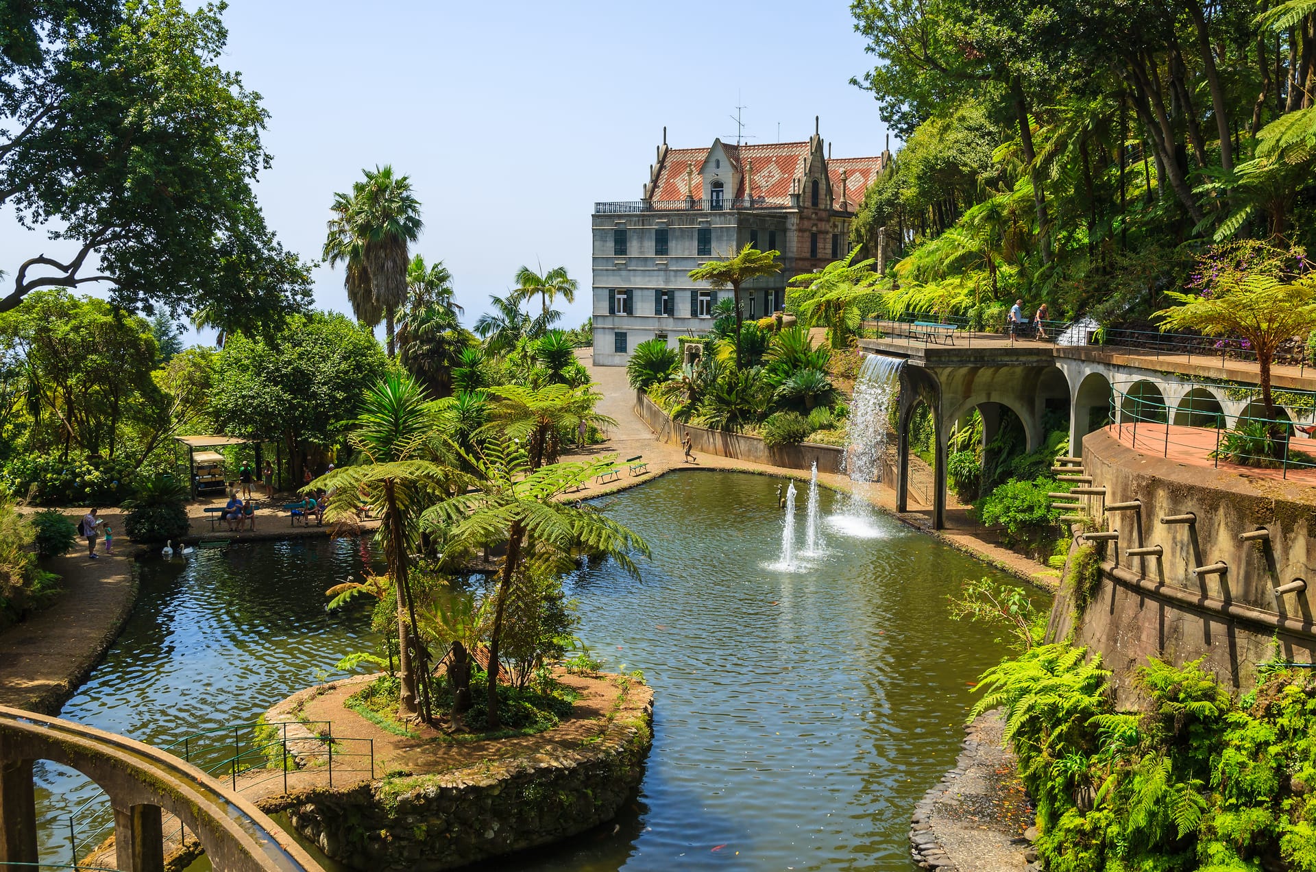 Lush botanical garden with pond, fountains, waterfall, and historic building in Madeira.