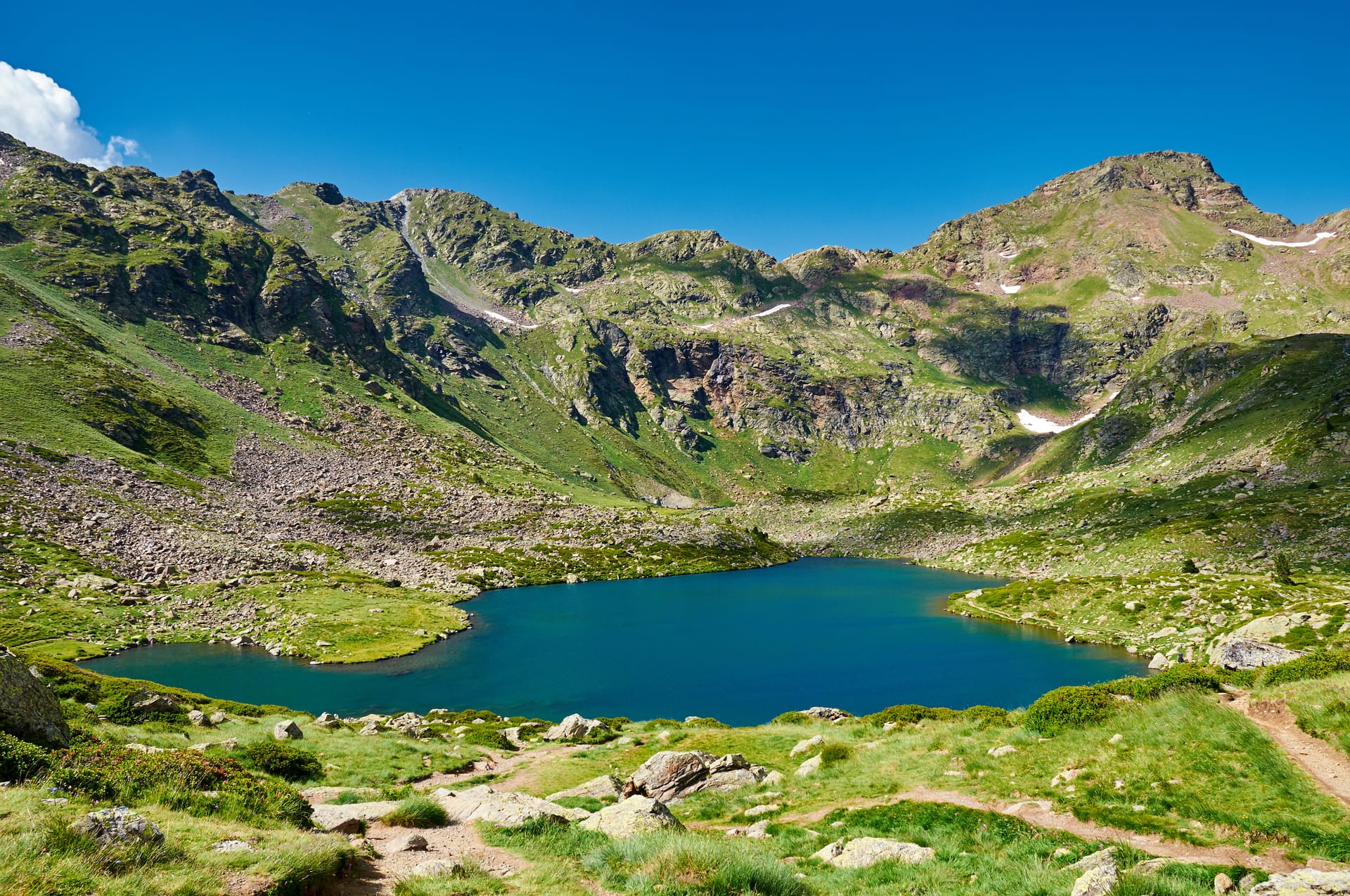 Alpine lake with deep blue water surrounded by green, rocky mountains under a clear blue sky.