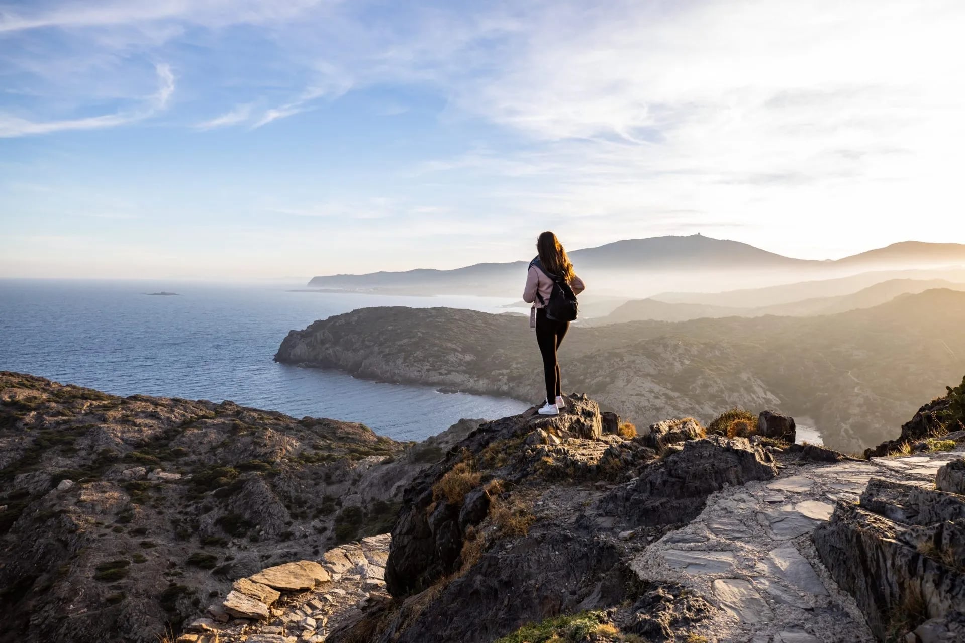 Walker standing on a rocky headland looking out over the sea at first light