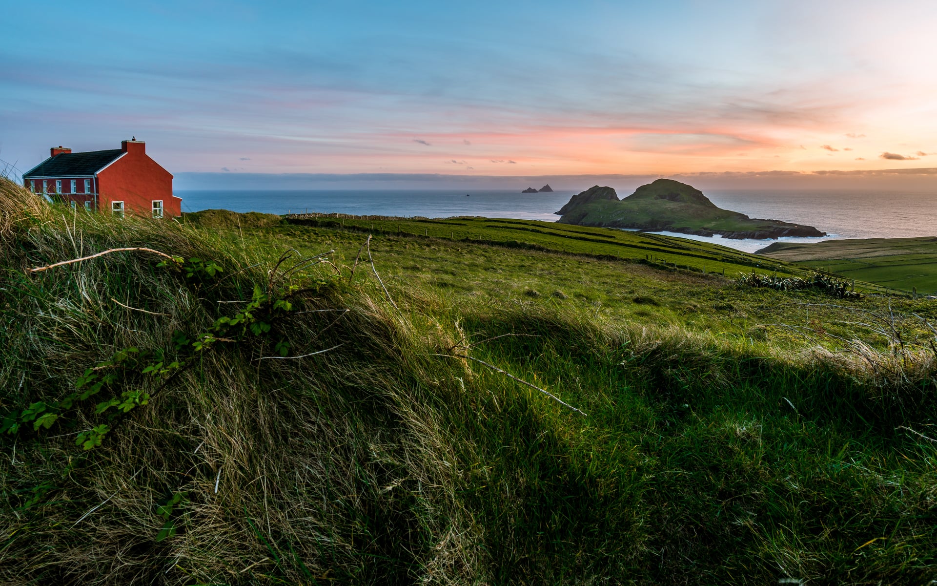 A red house on a clifftop at sunset with islands offshore on the Skellig ring