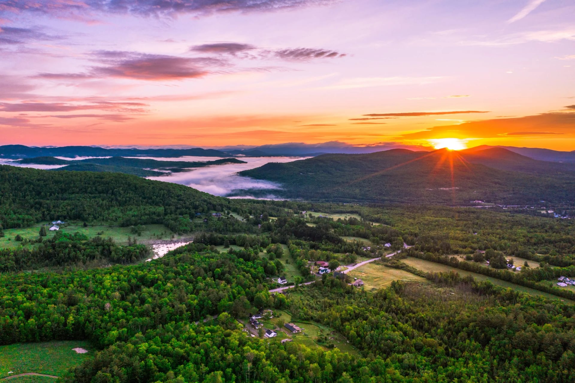 Sunrise over a wooded valley of farms and fields with mist lying in the hollows