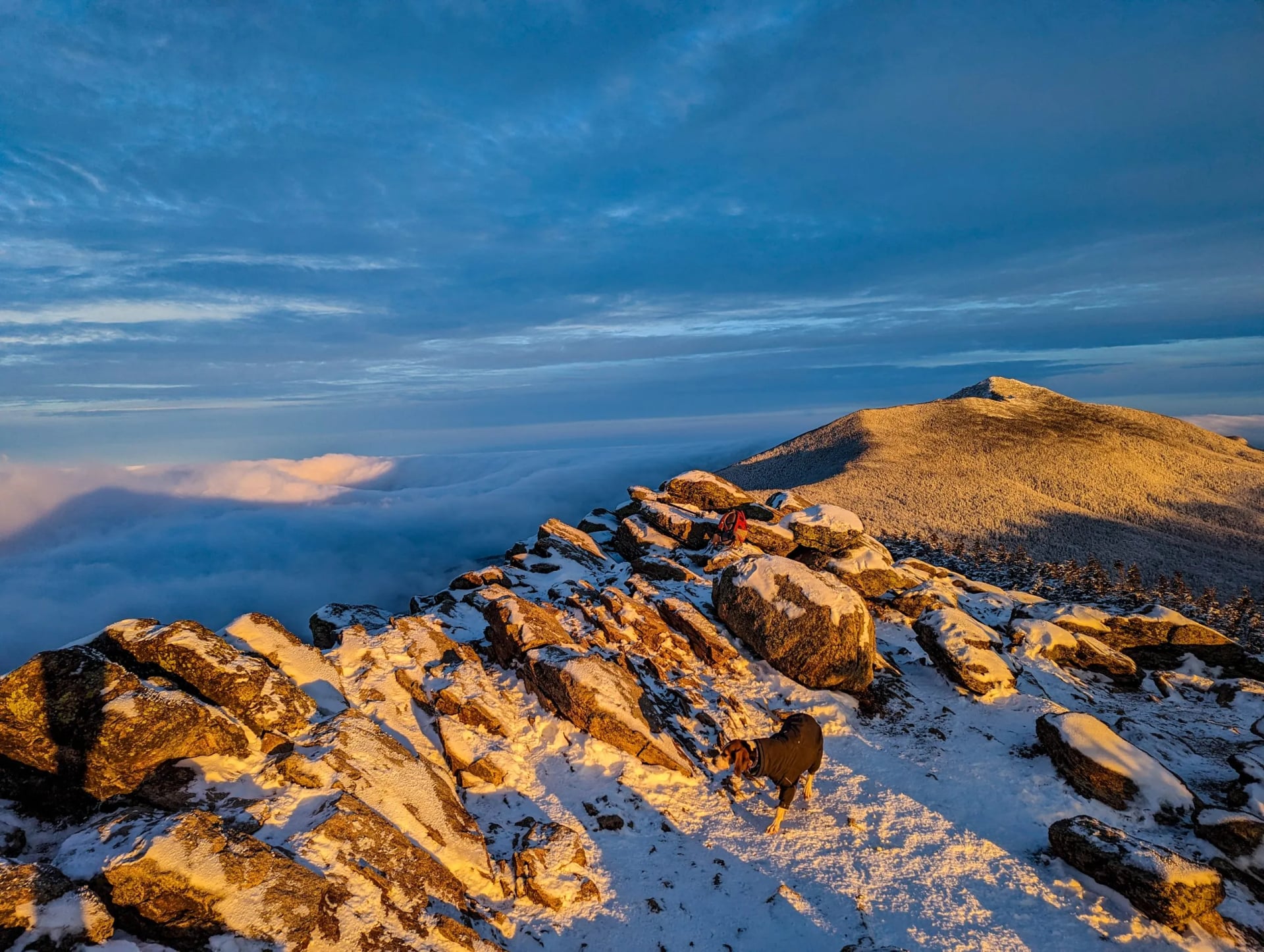 Low sun striking a rocky crest dusted with snow above a cloud layer