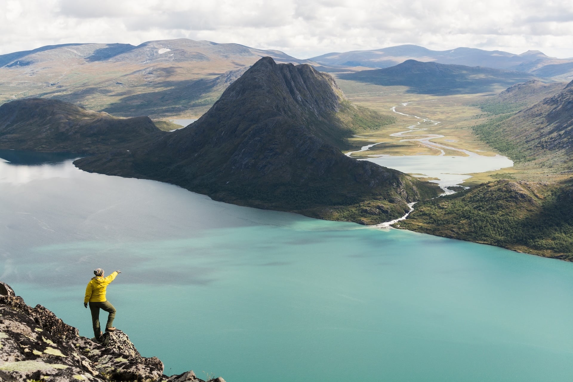 Hiker on Besseggen ridge pointing over turquoise lake and mountains in Norway.