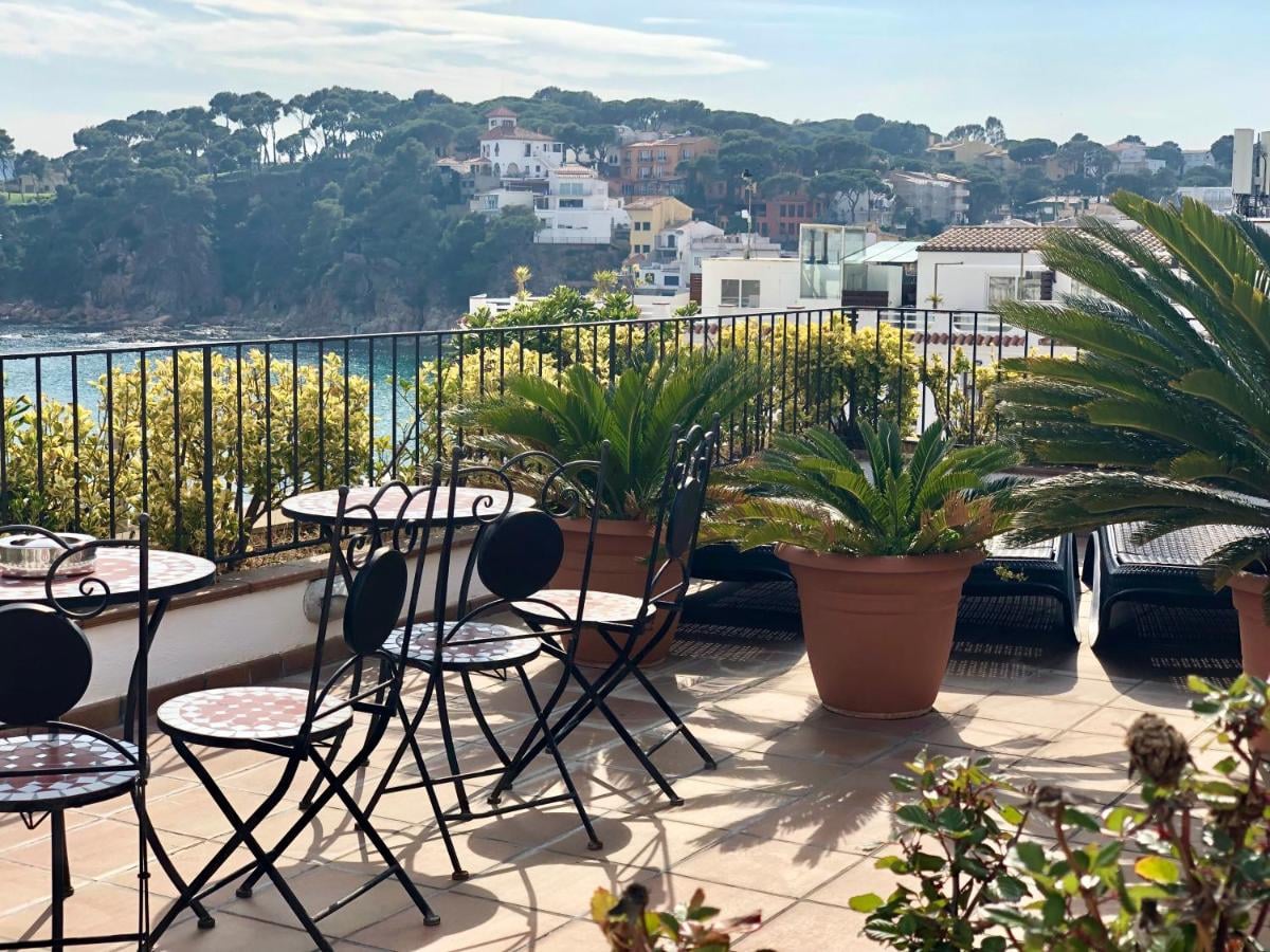 Cafe tables on a shaded terrace looking down over a bay and white houses