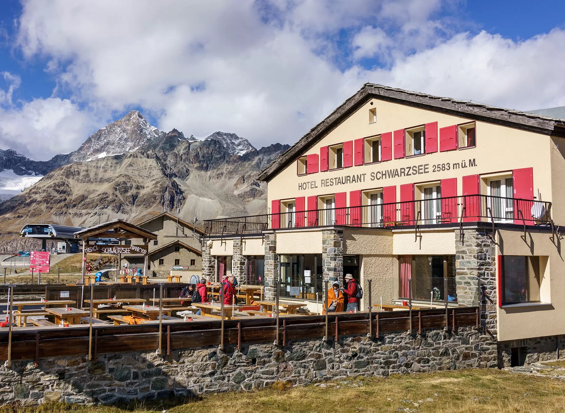 Een berghotel met rode luiken en een houten terras onder de top