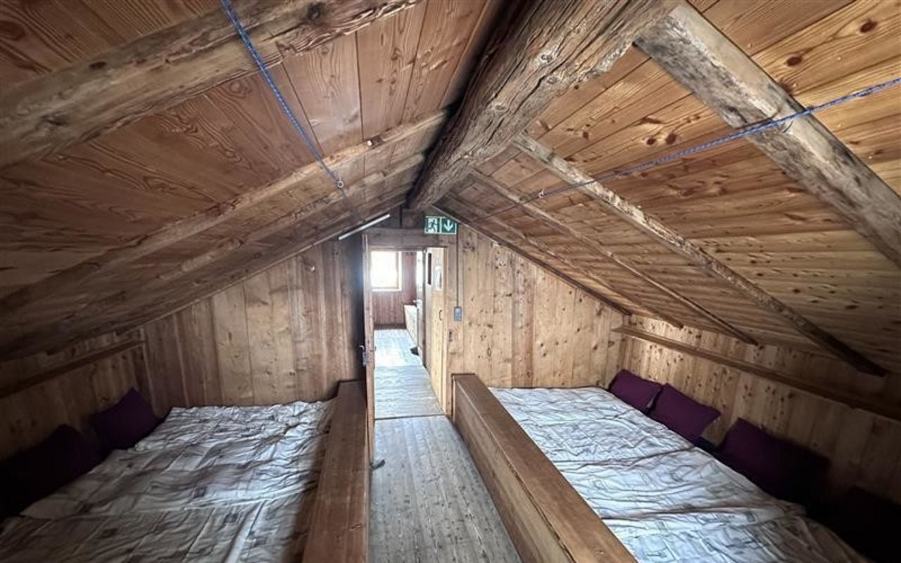 Een lange houten slaapplatform onder een houten dak in een slaapzaal van een berg hut